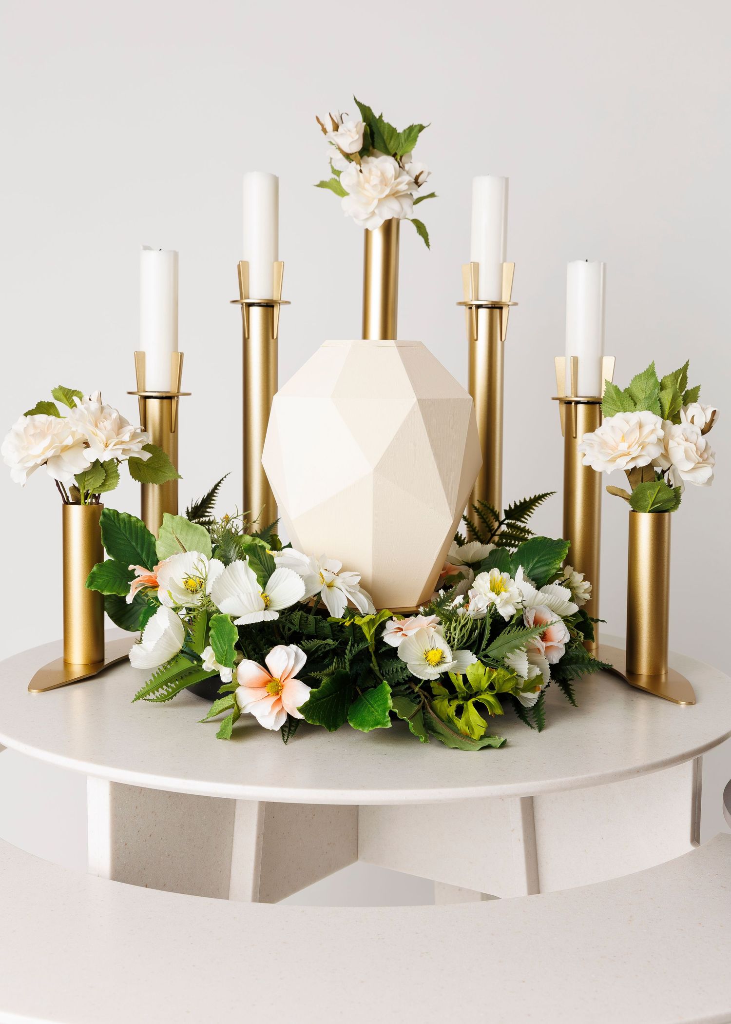 Modern white and gold candlesticks arranged with fresh flowers on floating shelf.