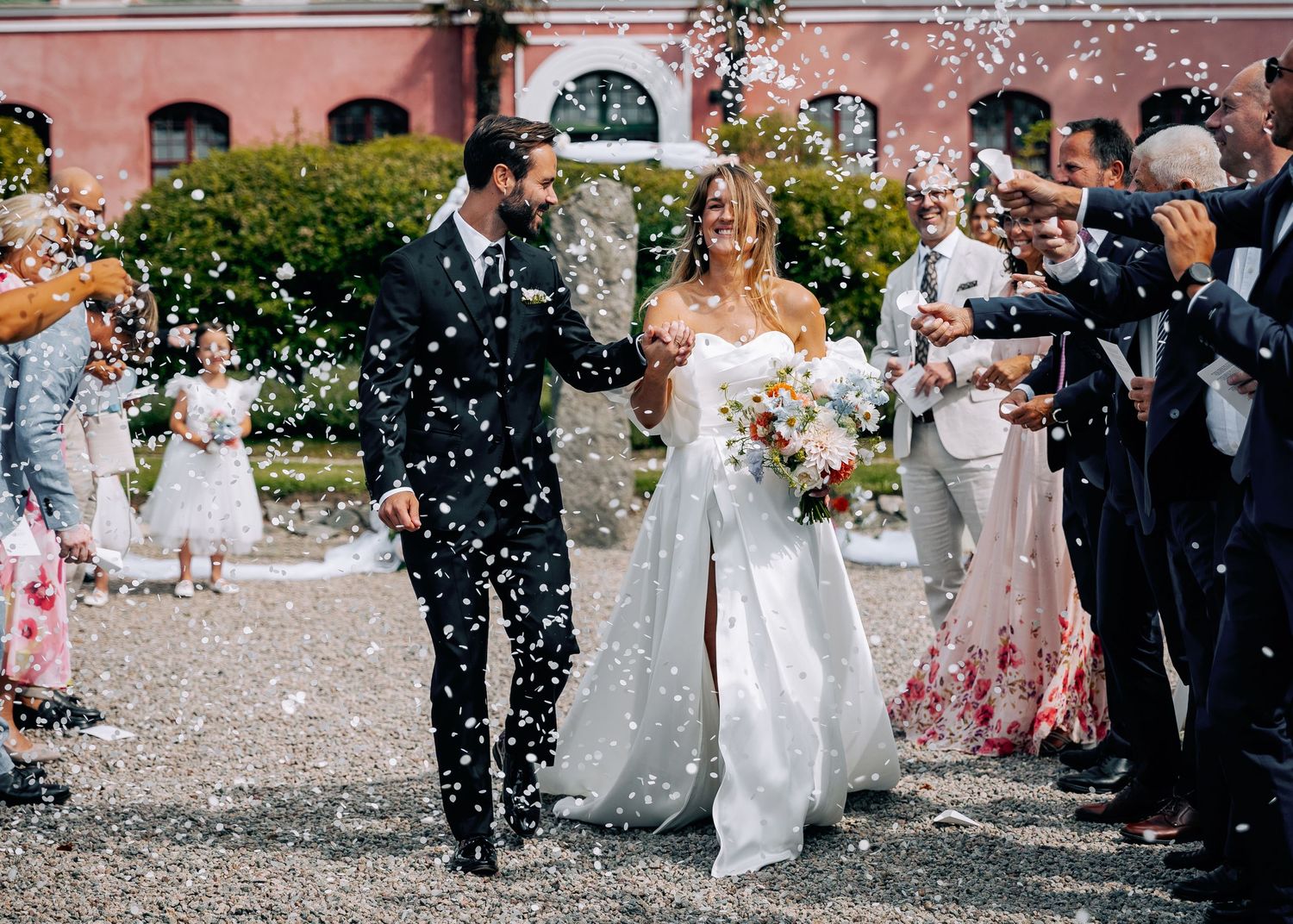 Joyful wedding exit with guests throwing confetti at couple on gravel path.