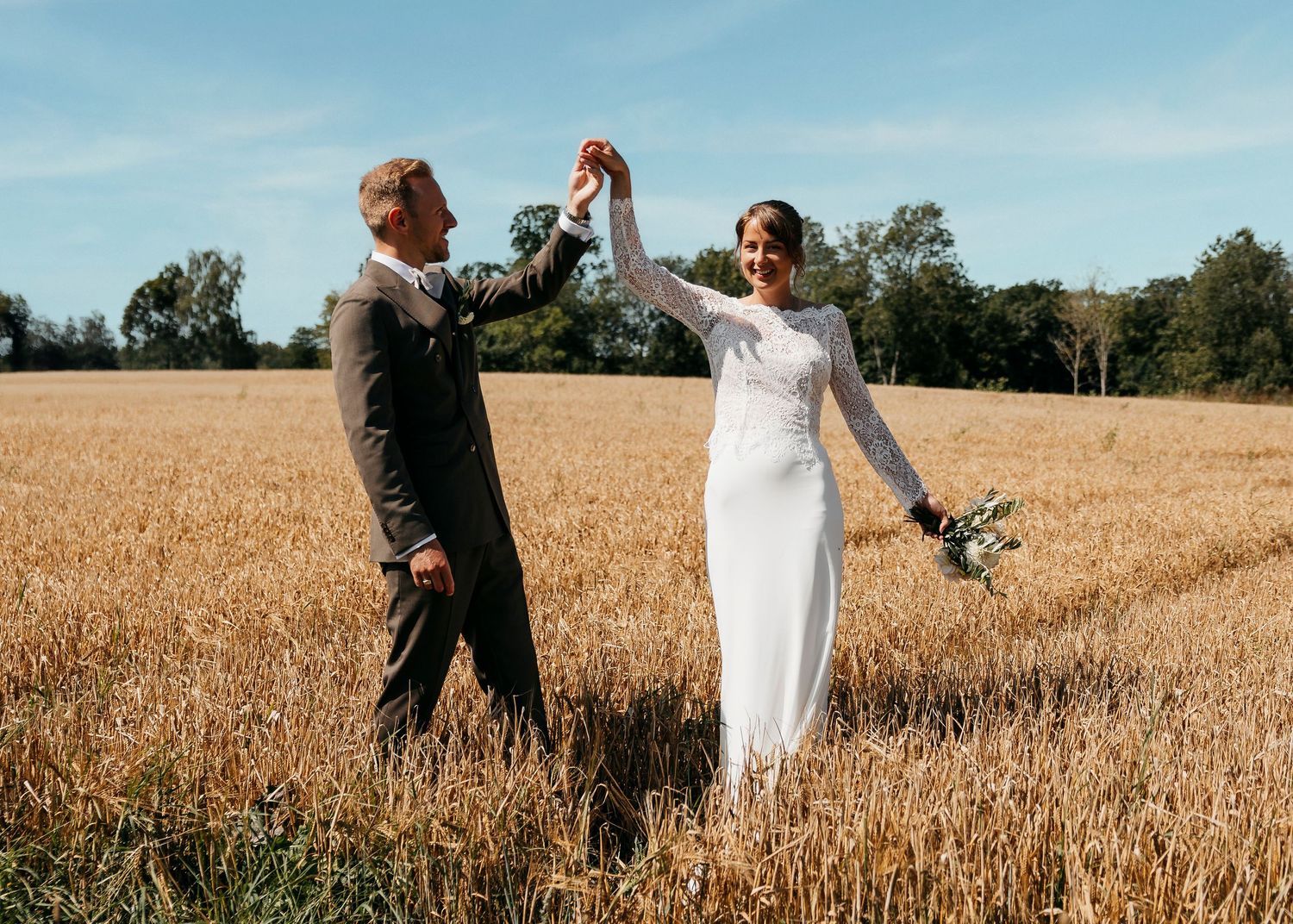 Wedding couple stands together in a golden wheat field under blue summer sky.
