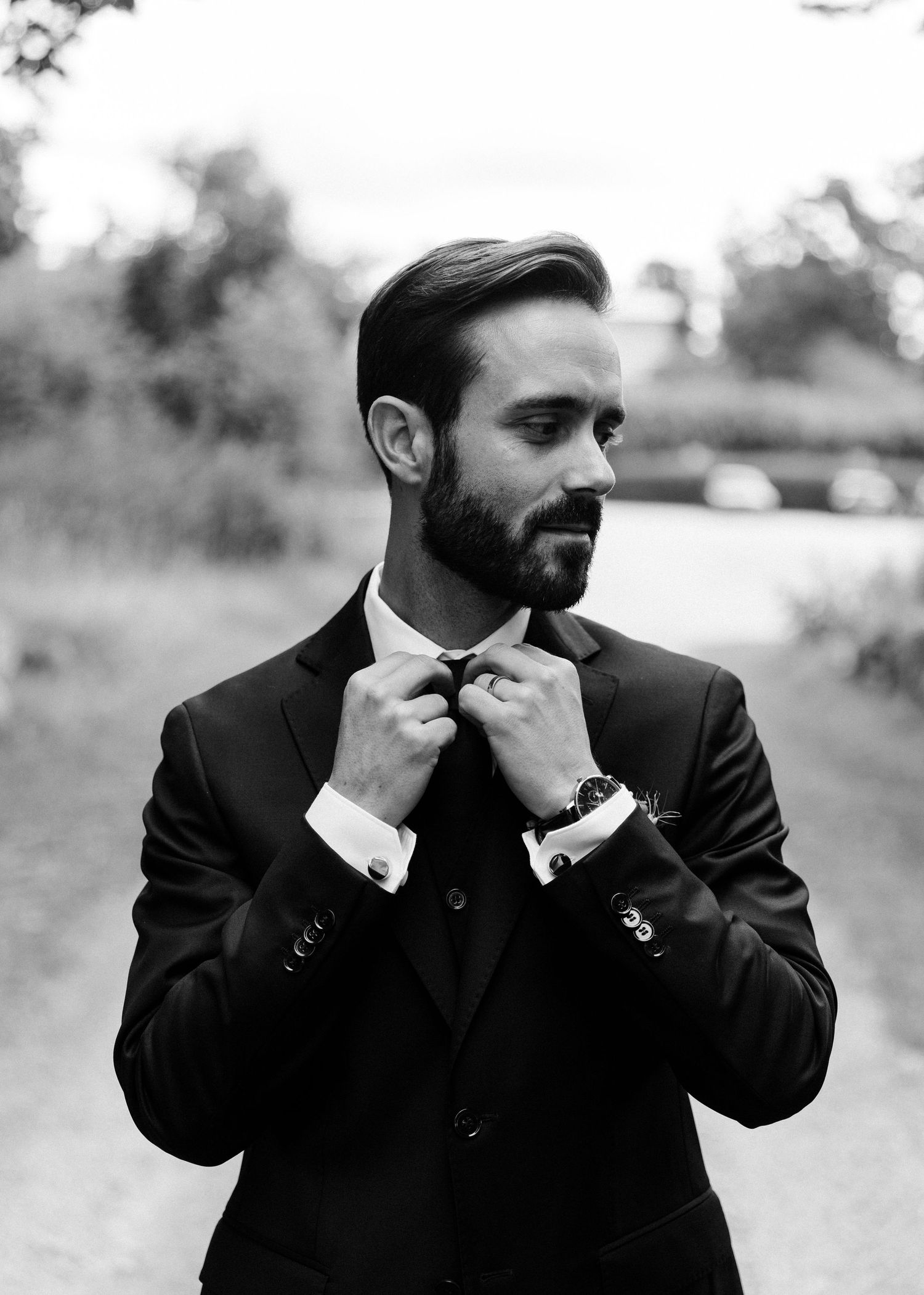Black and white portrait of groom adjusting bowtie in formal suit.