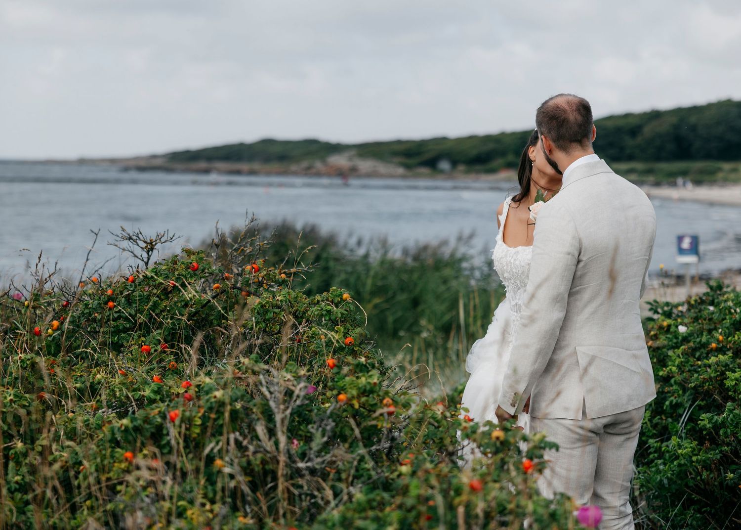 Wedding couple walks along coastal path with wildflowers.