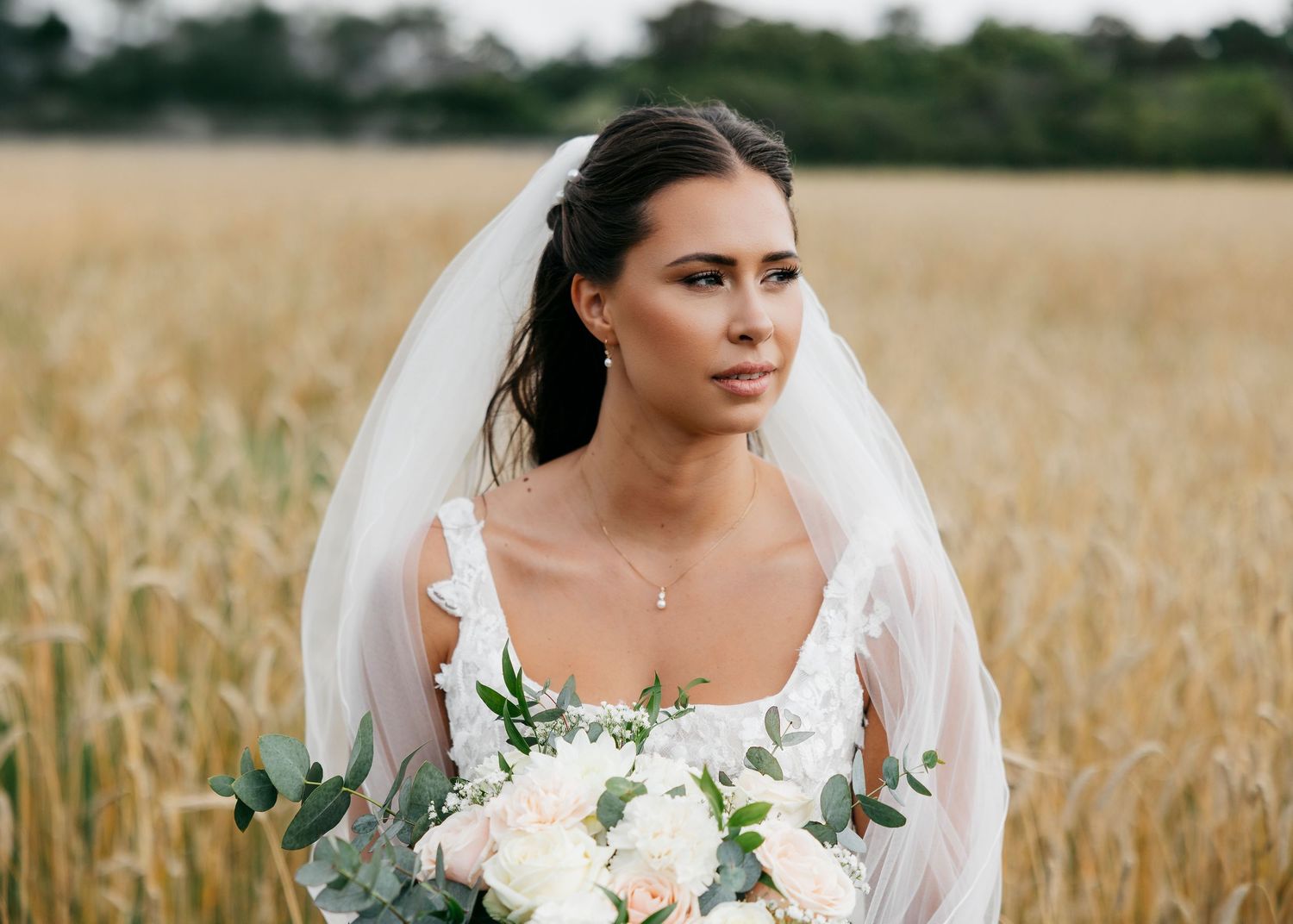 Close-up portrait of bride with white bouquet in wheat field.