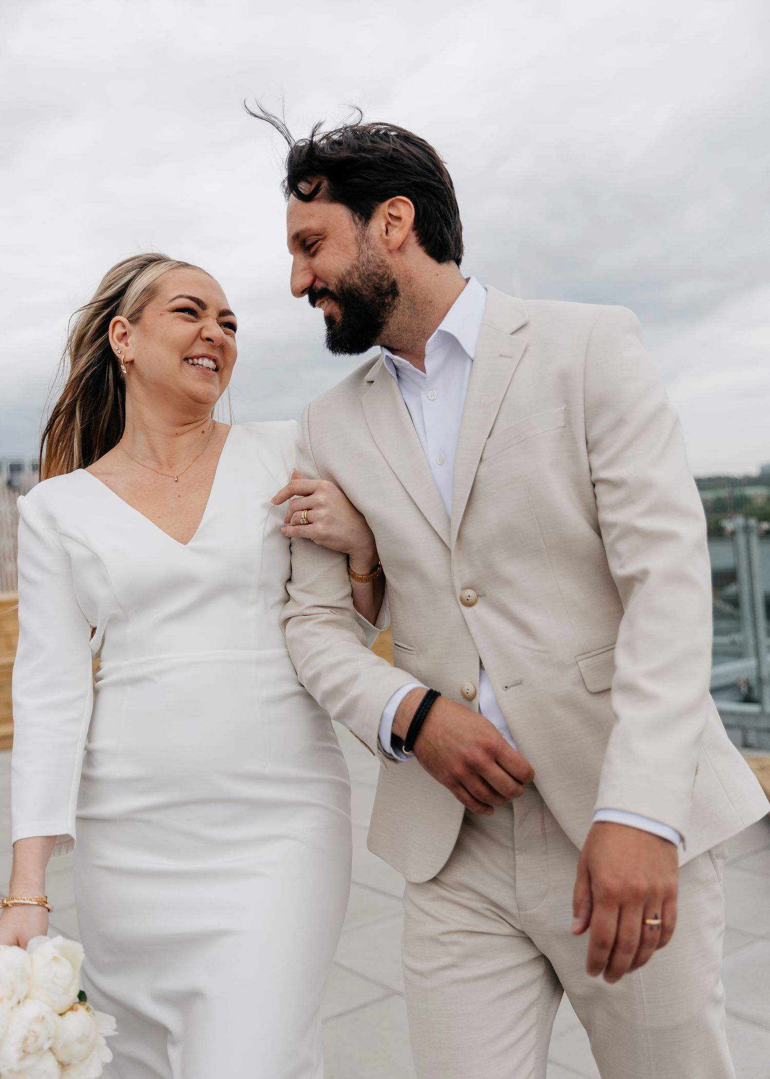 Bride in white dress and groom in beige suit share tender moments during seaside photoshoot.