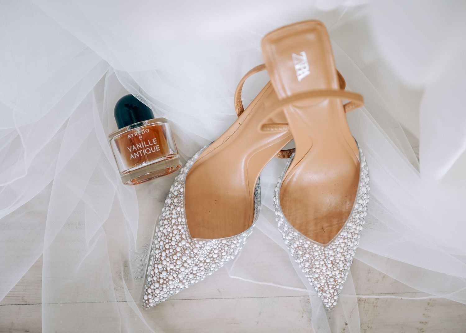 Pearl-encrusted bridal shoes and nail polish displayed with tulle veil.