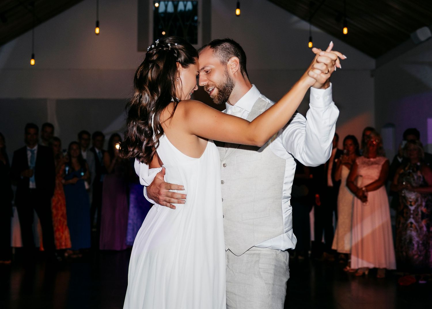 A couple shares their first dance at a wedding reception under warm lighting.
