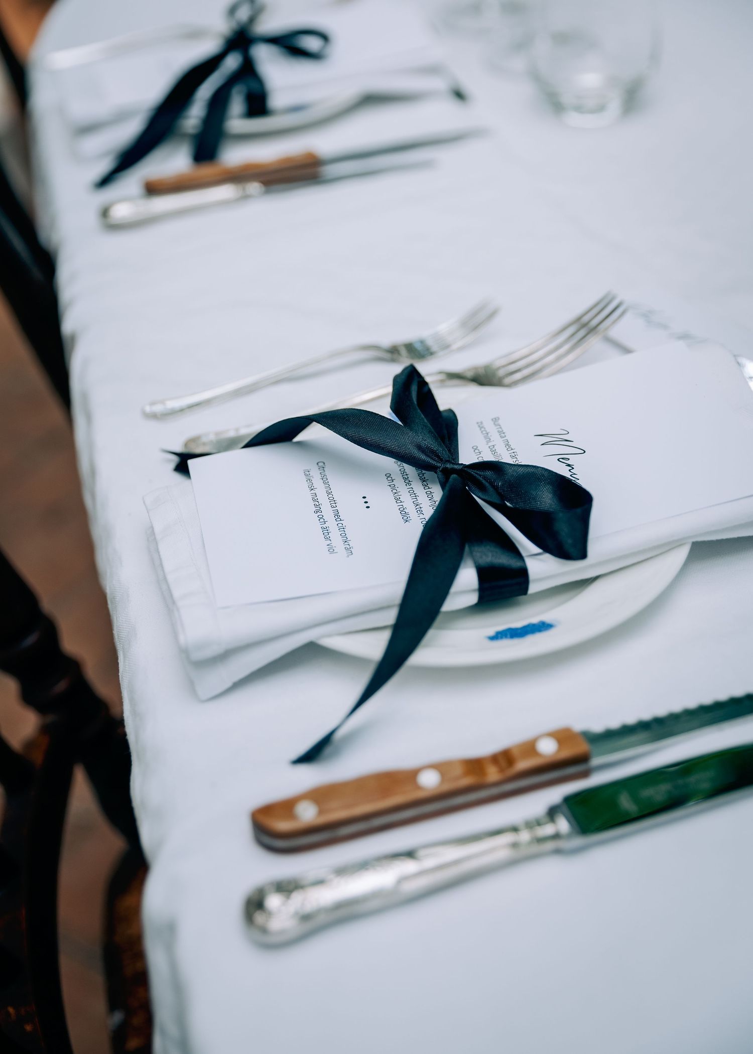 Wedding place settings with white plates and navy blue ribbons on crisp tablecloth.