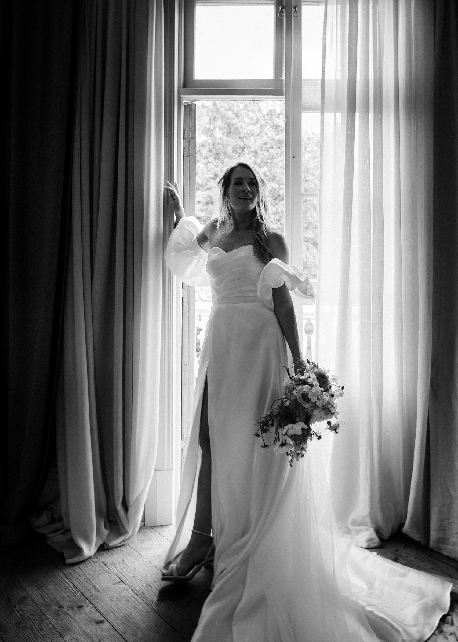 Elegant black and white bridal portraits by window with flowing curtains and natural light.