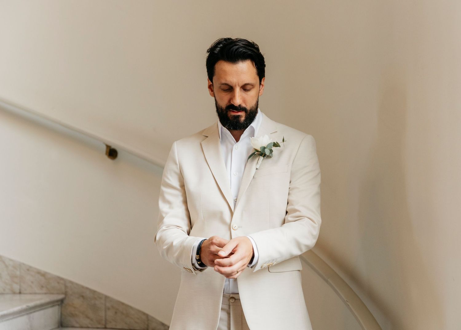 A series of shots showing a groom in a cream suit adjusting his cuffs and getting ready.