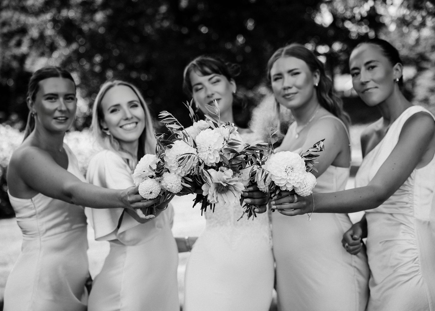 Wedding party members embrace and laugh together in black and white photography.