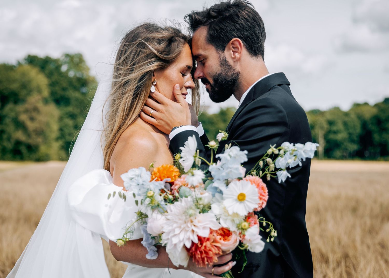 Wedding couple embraces while holding a vibrant bouquet of flowers in an outdoor setting.
