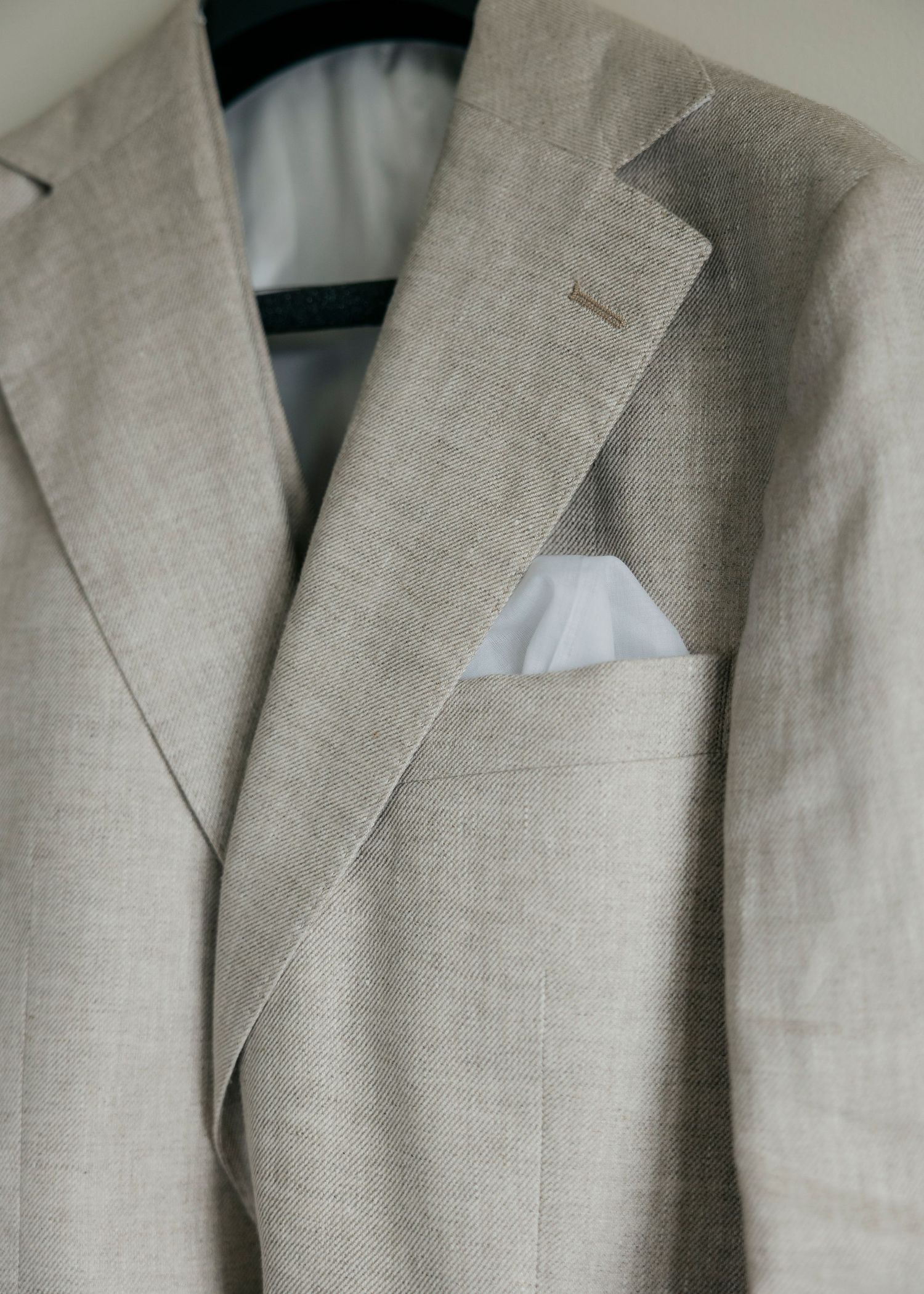 Row of light beige linen suit jackets hanging on clothing rack.