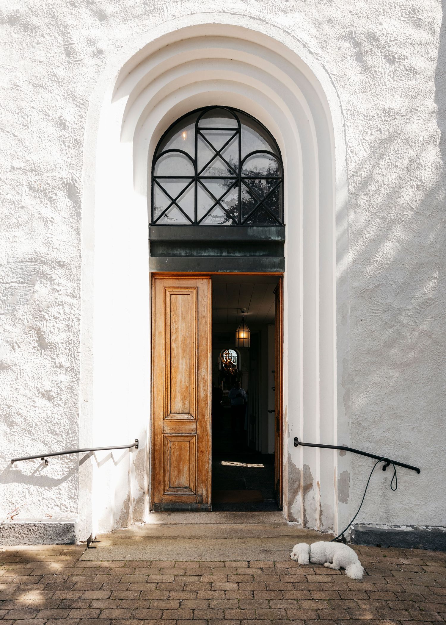 White church entrance with arched doorways and wooden doors on brick steps.