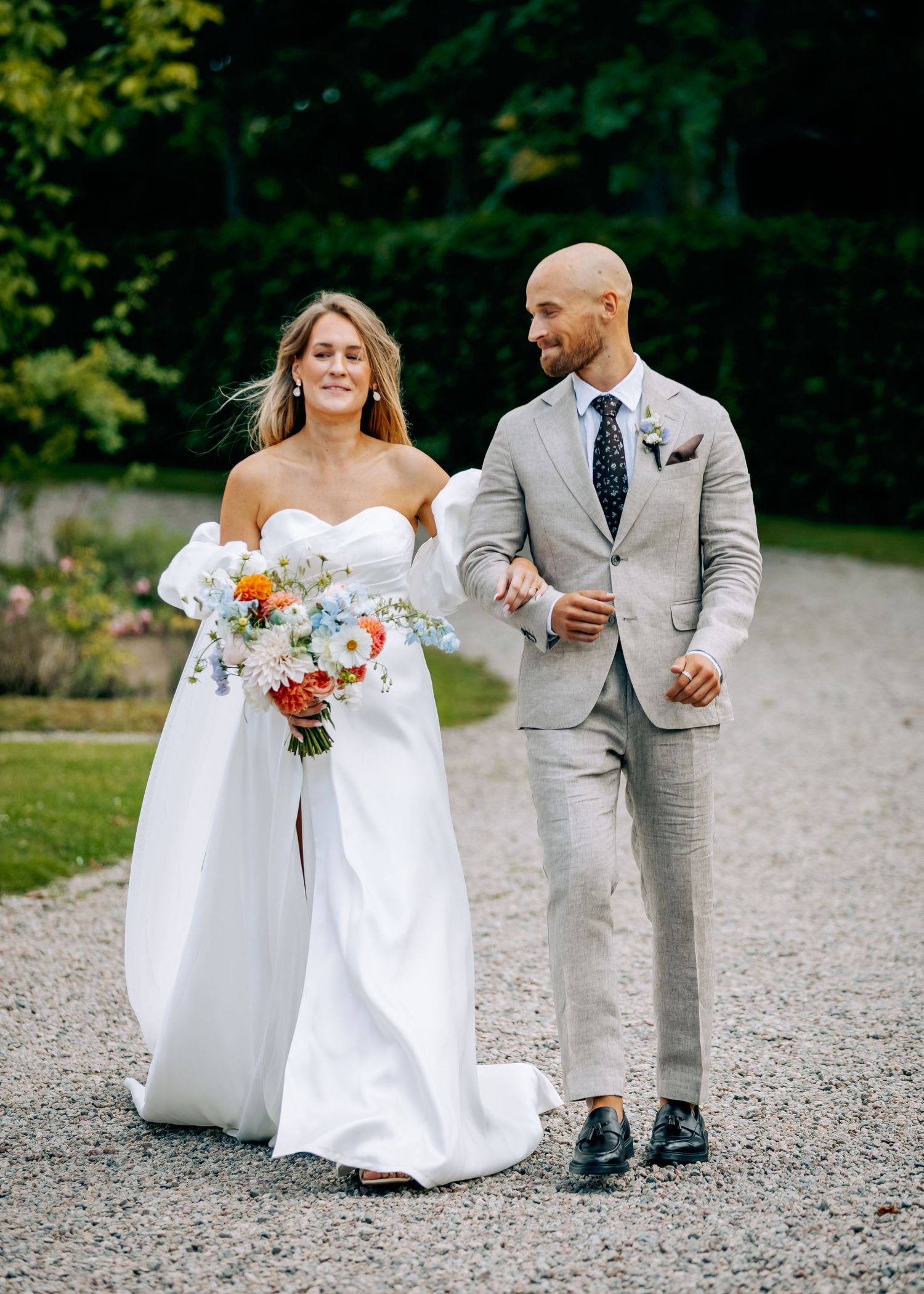 Wedding party walking on a gravel path with white dresses and light gray suits.
