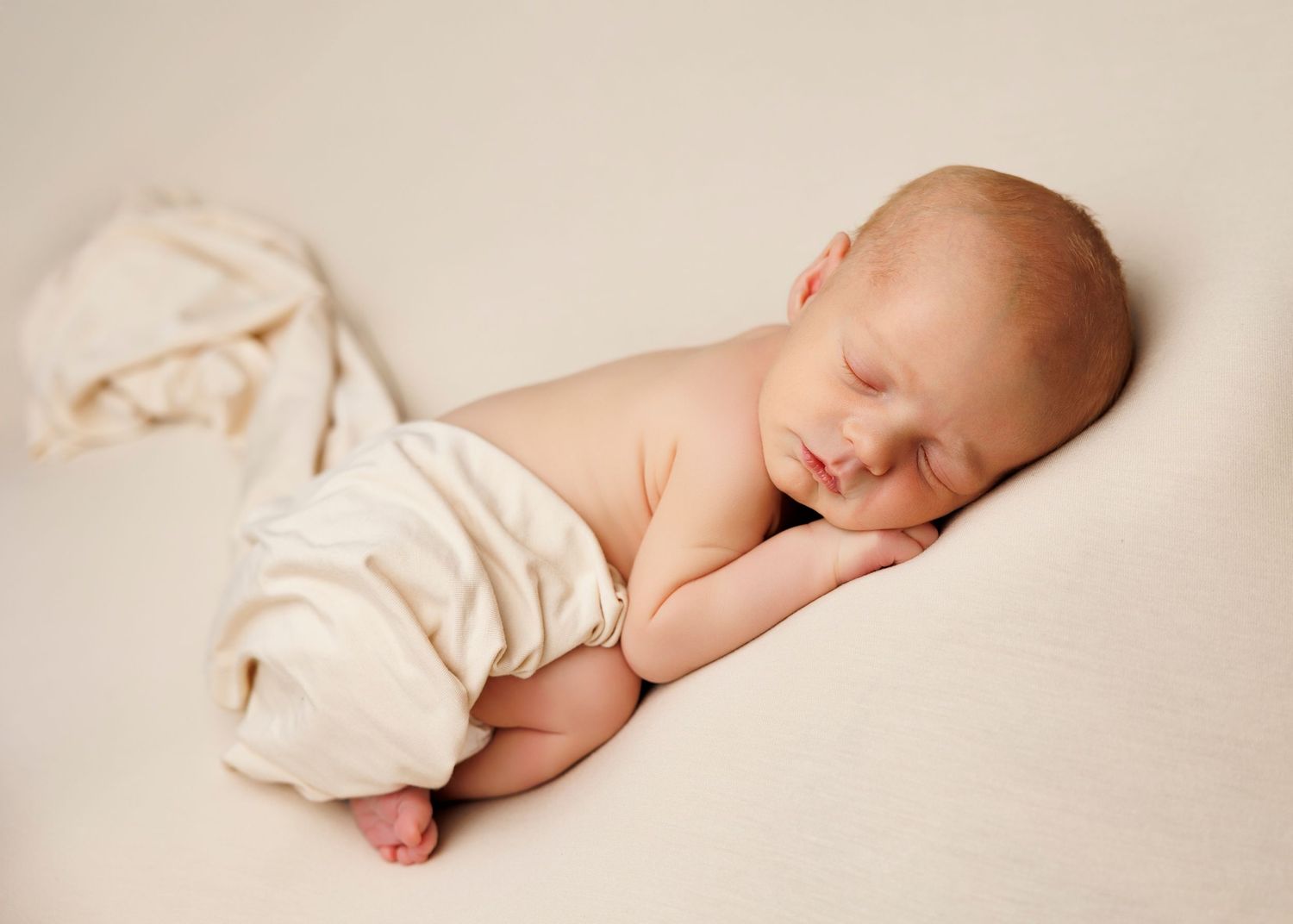 A series of soft, minimalist photographs showing a sleeping newborn baby in gentle beige tones.