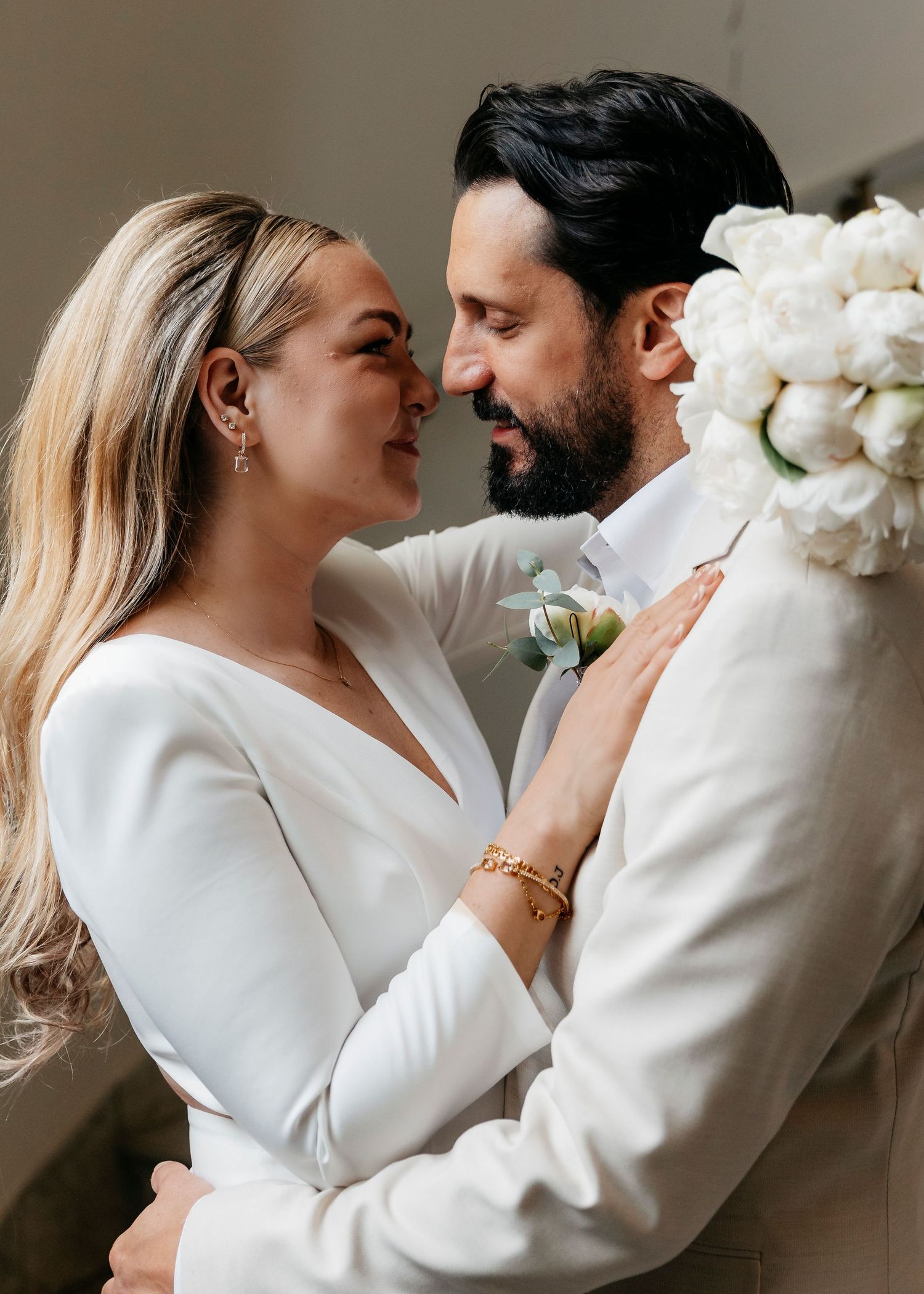 A series of candid moments between a couple in white formal wear against a neutral wall.