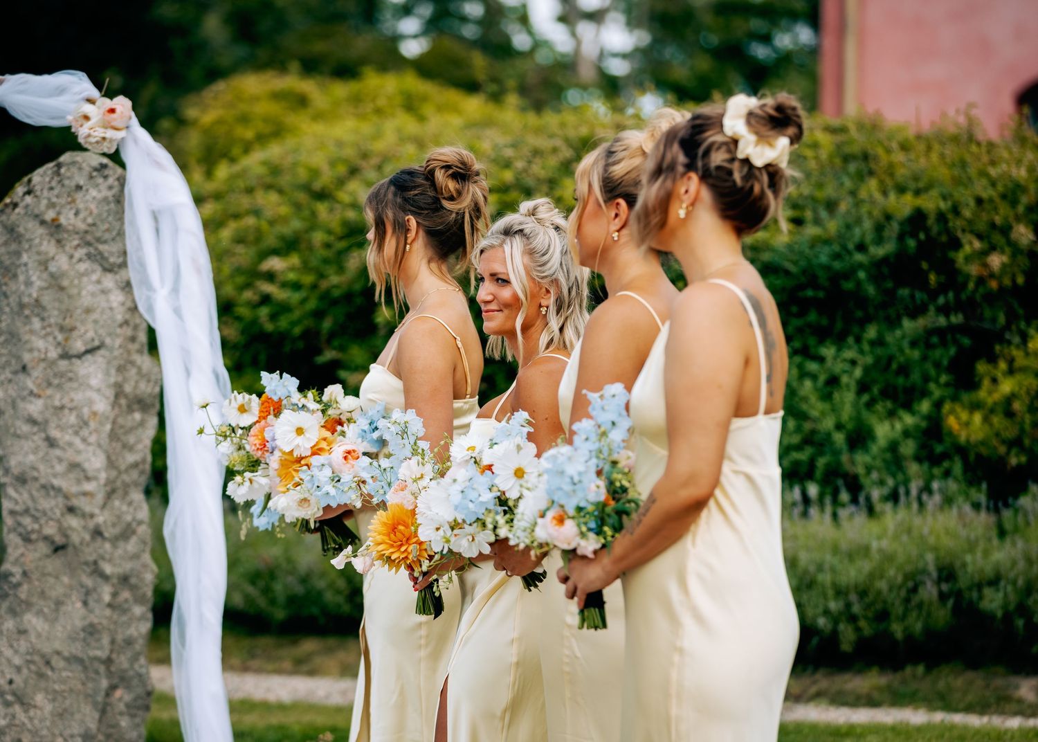 Wedding party members holding colorful bouquets against pink building backdrop.