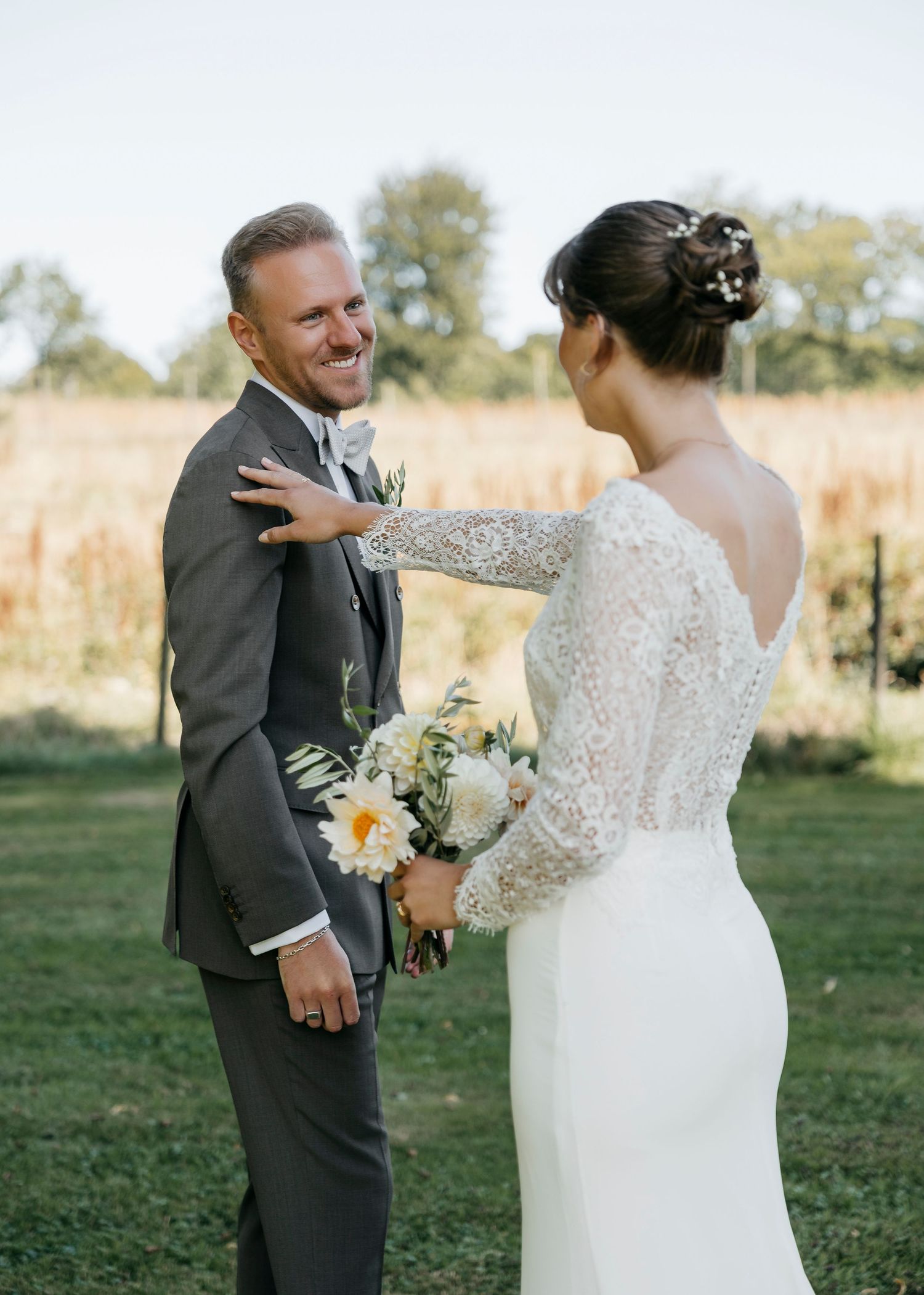 Newlyweds share a joyful moment in an outdoor setting with sunlit fields in the background.
