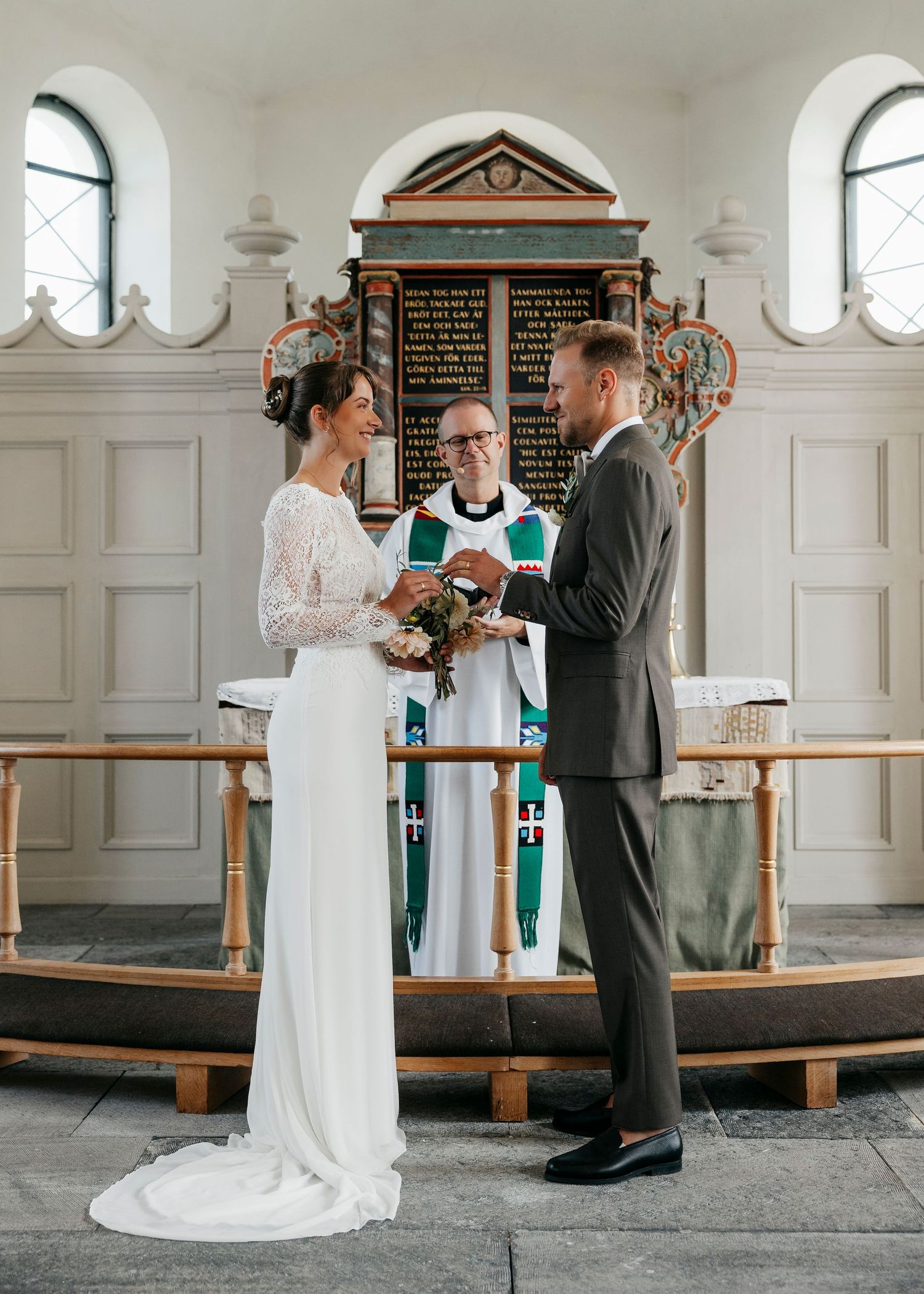 Wedding ceremony in progress inside historic white church with wooden details.