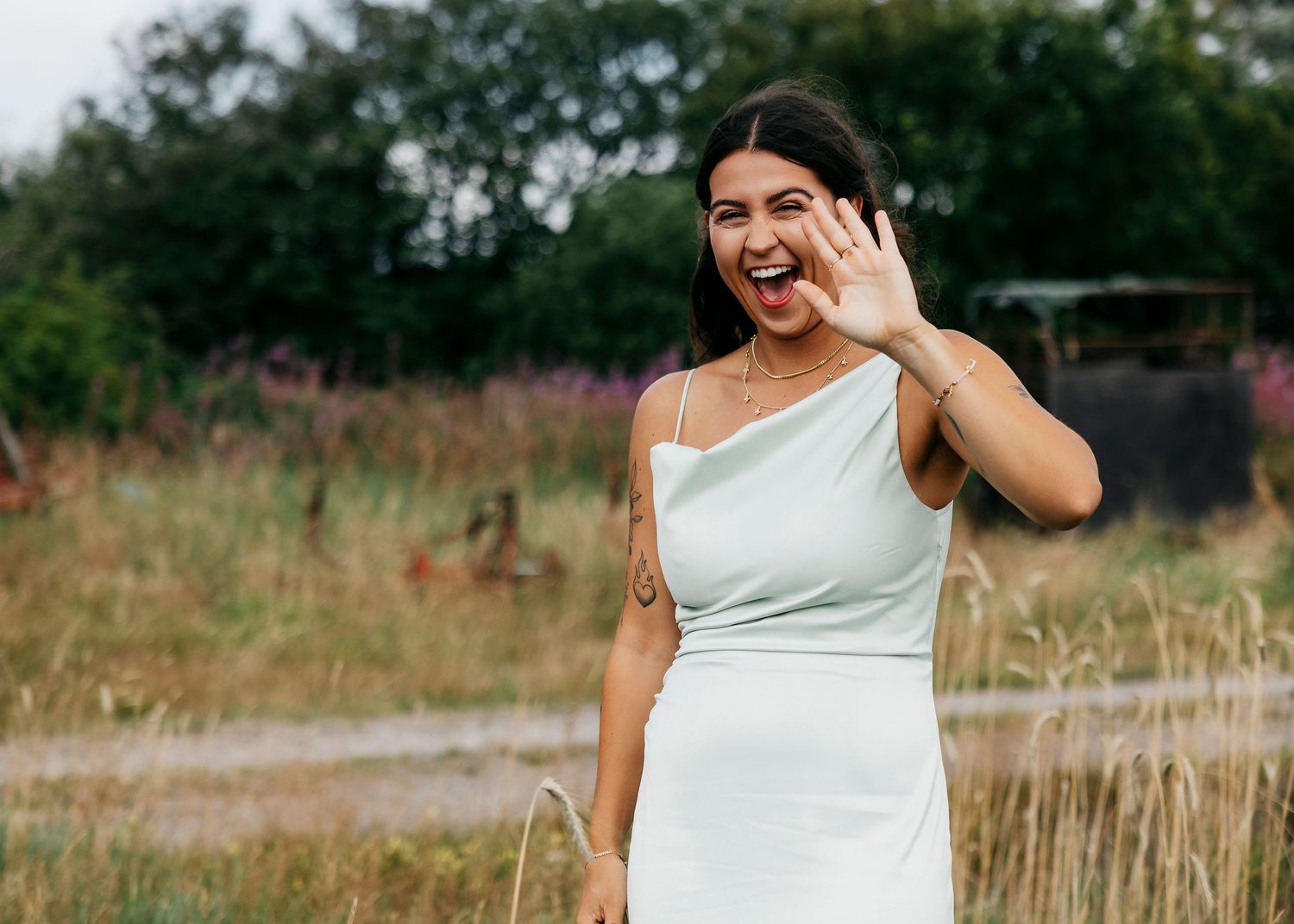 Wedding party laughs together while standing in a field of tall grass.