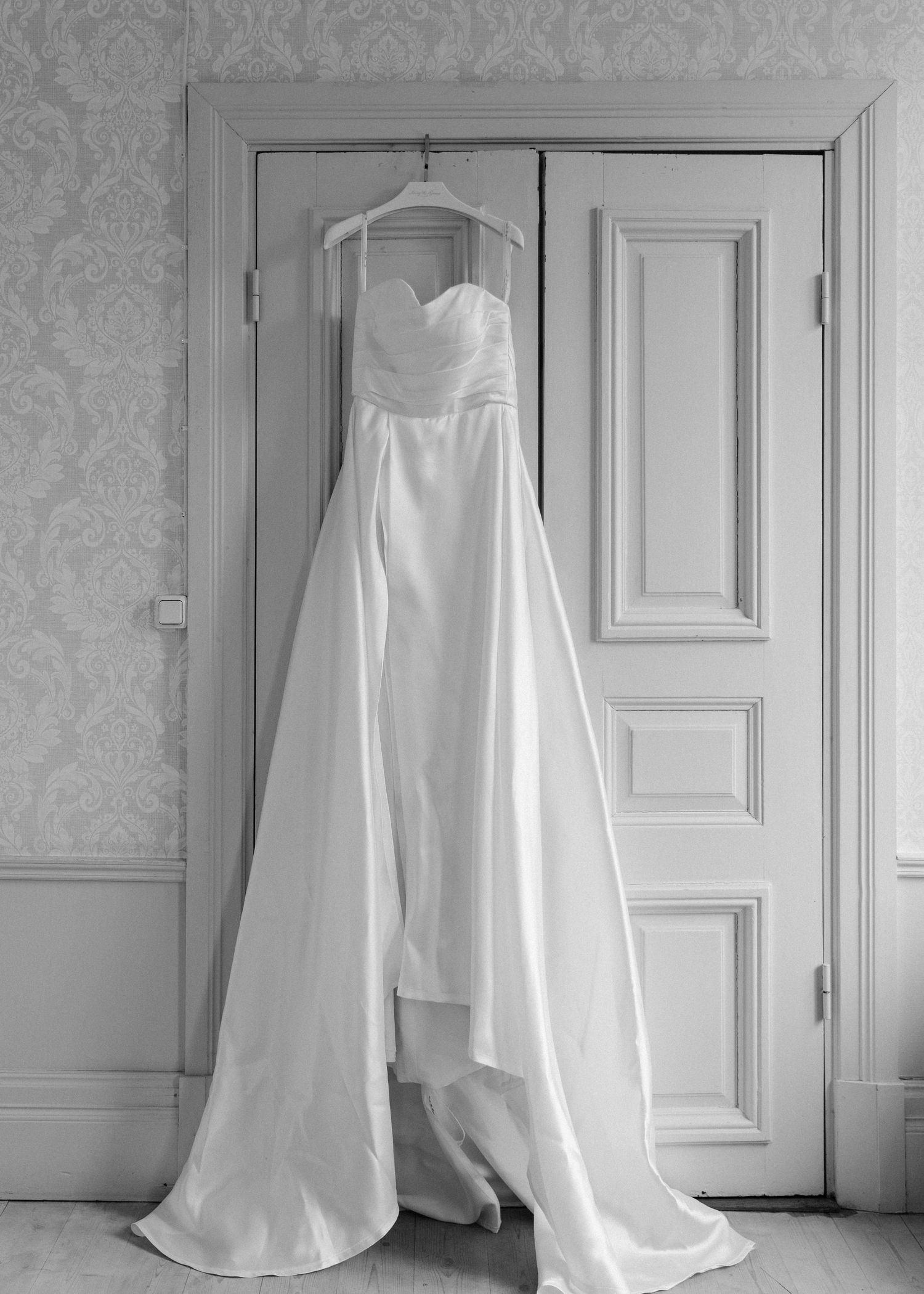 White wedding dress hanging on door with sweetheart neckline and flowing train.