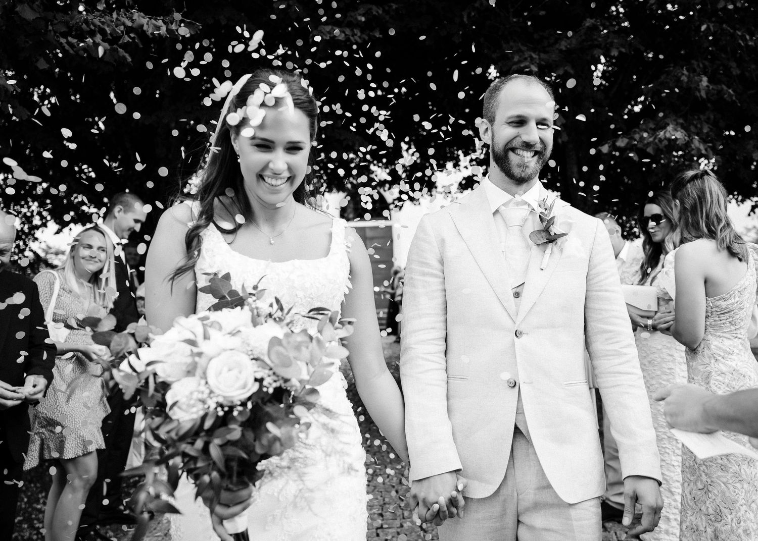 Black and white photo of wedding celebration with confetti toss outdoors.