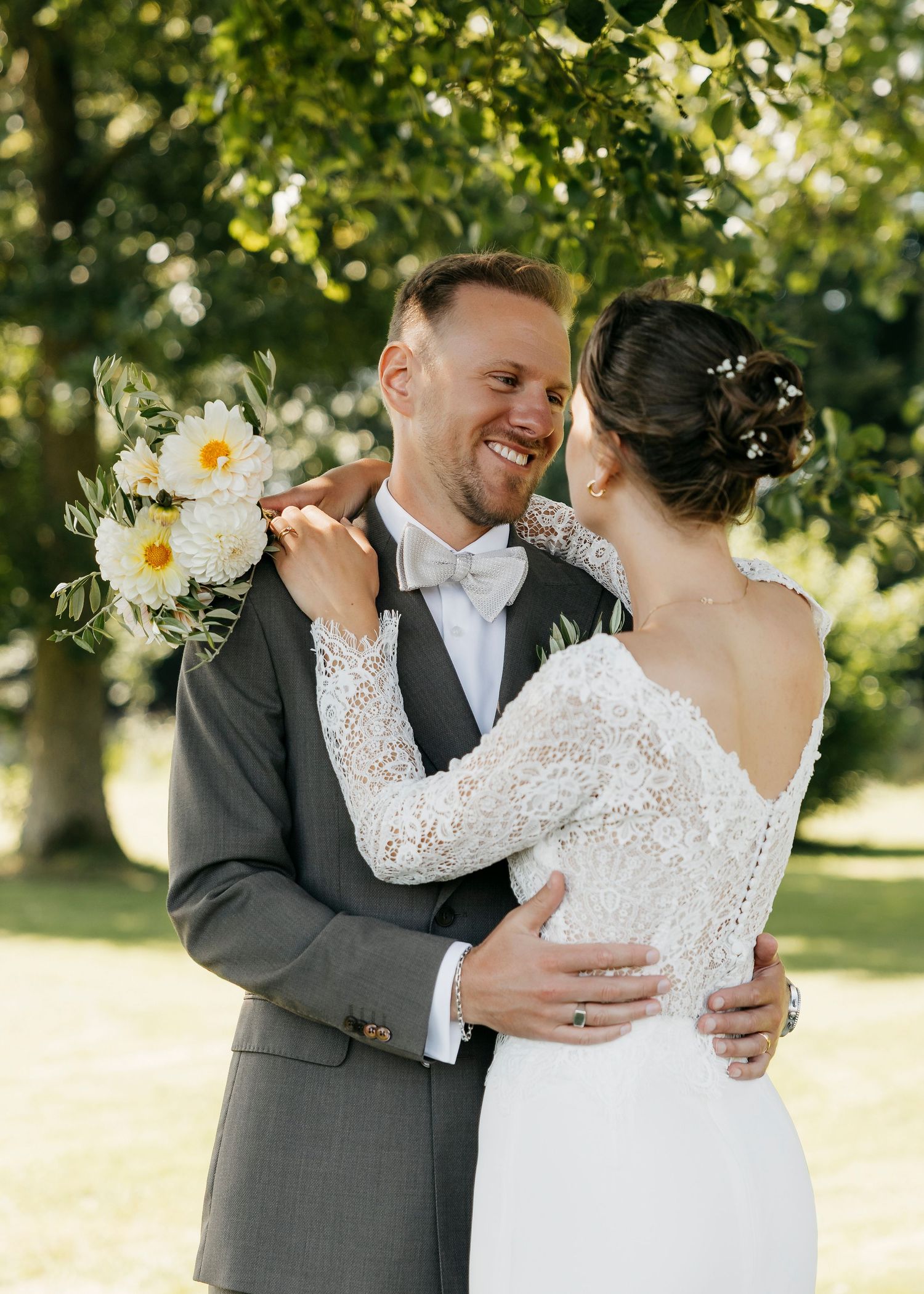 Intimate wedding portraits captured in golden sunlight beneath leafy green trees.