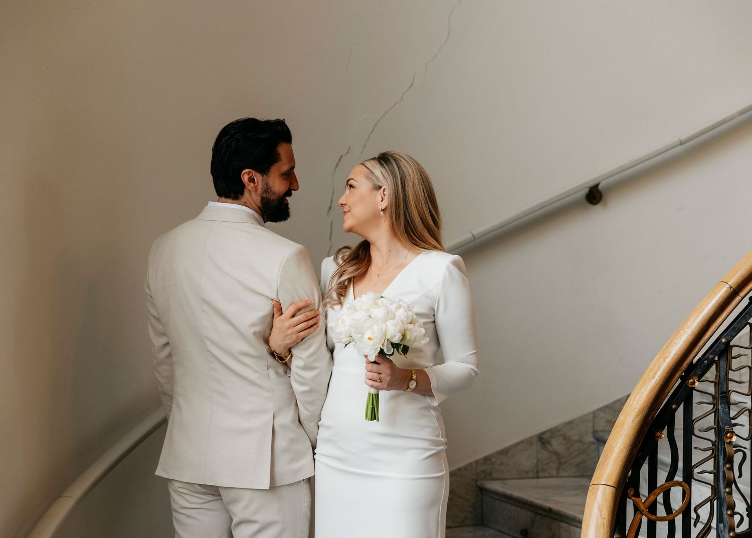 A romantic couple in matching white attire shares an intimate moment on a staircase.