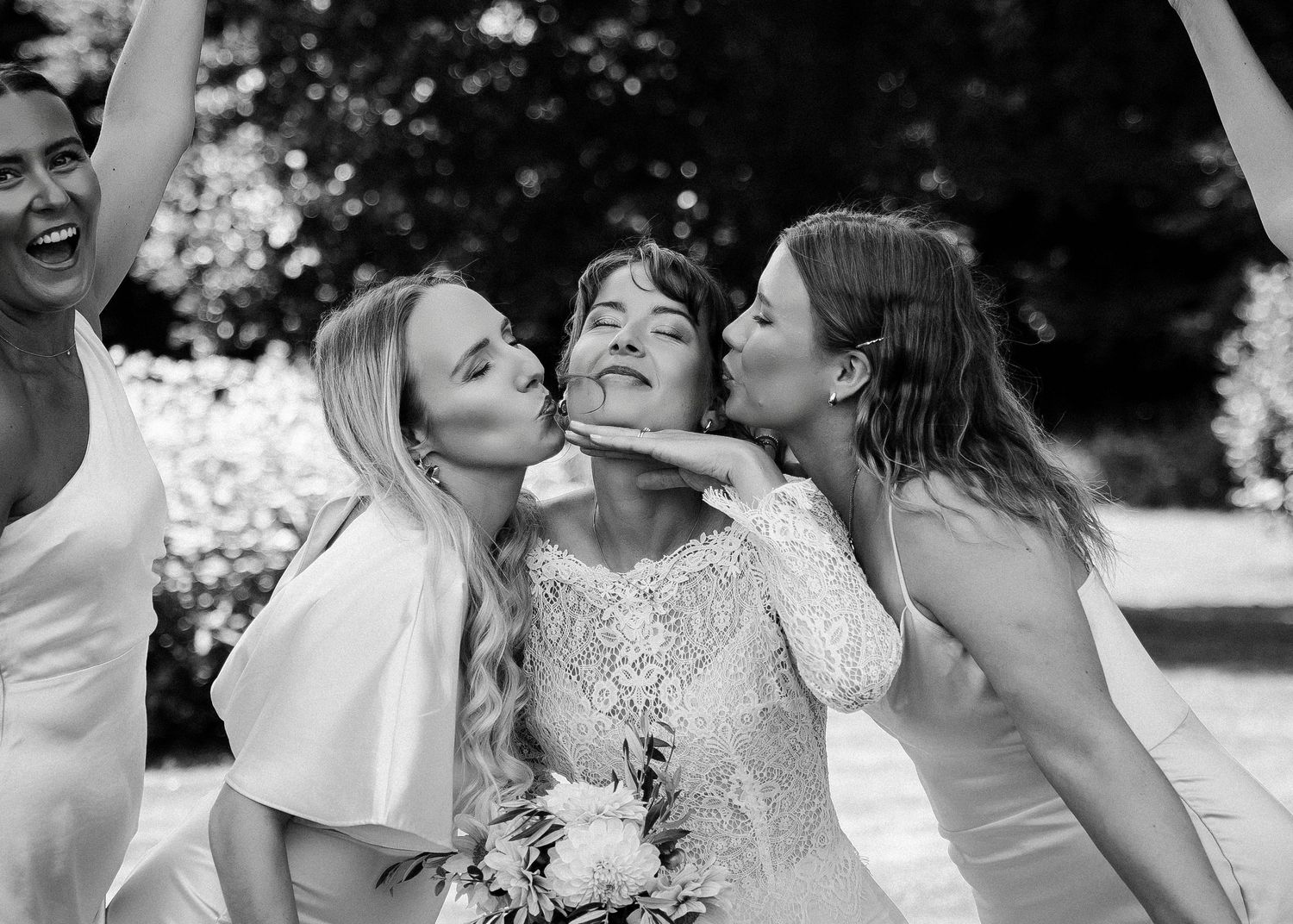 Wedding party members in white dresses and gray suits share joyful moments during outdoor photo session.