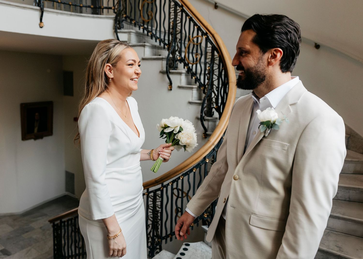 A couple in white and cream attire shares a romantic first look moment on a staircase.