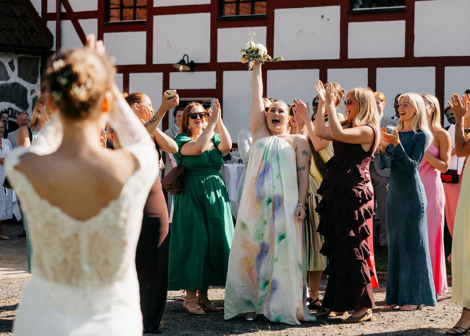 Wedding celebration scene with guests in colorful dresses outside a traditional building.