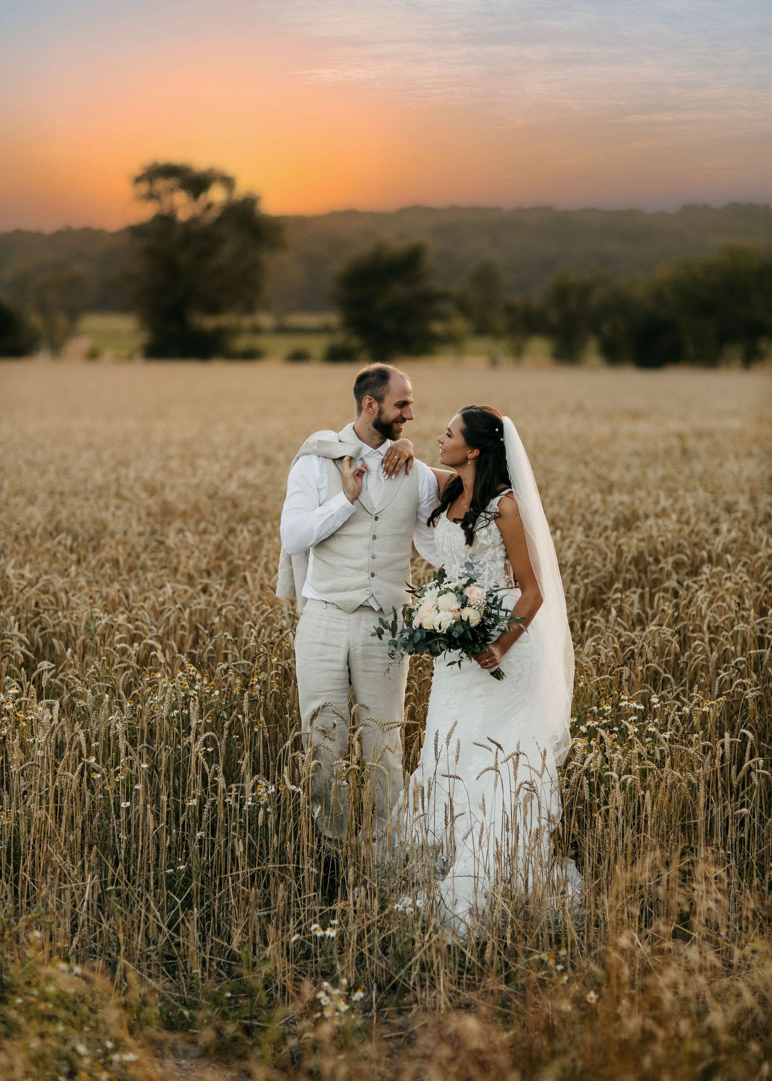 Newlyweds standing together in a golden wheat field at sunset.