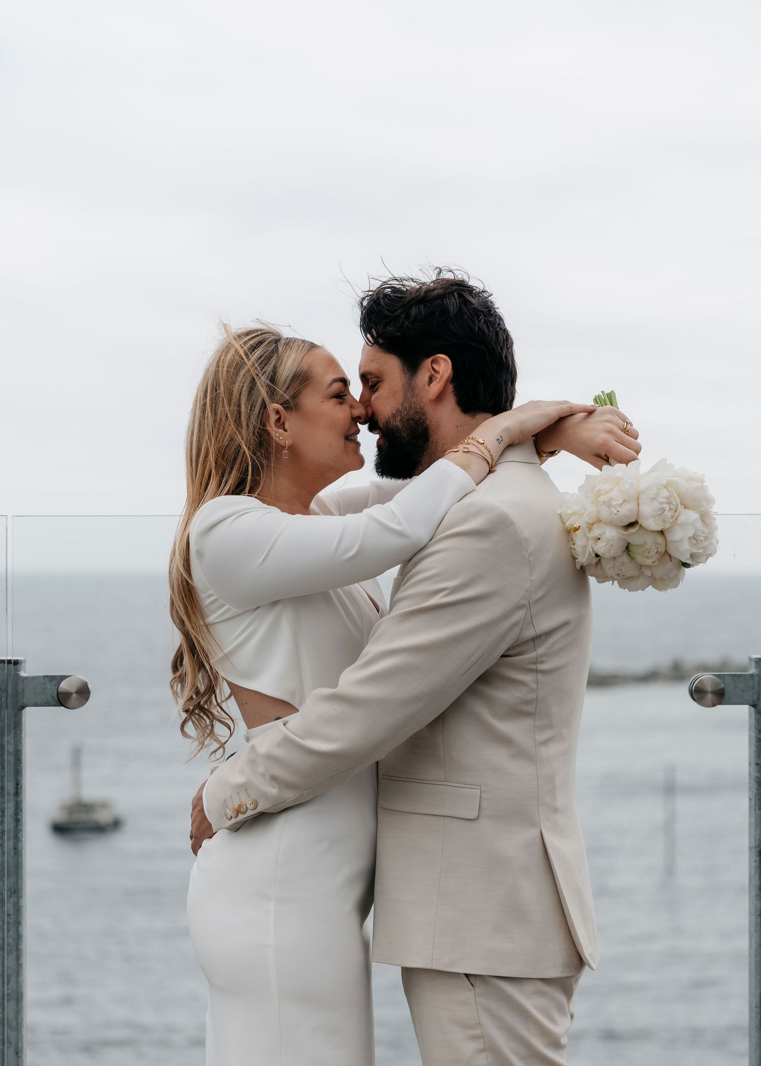 Romantic wedding couple sharing kisses against a seaside backdrop with white flowers.