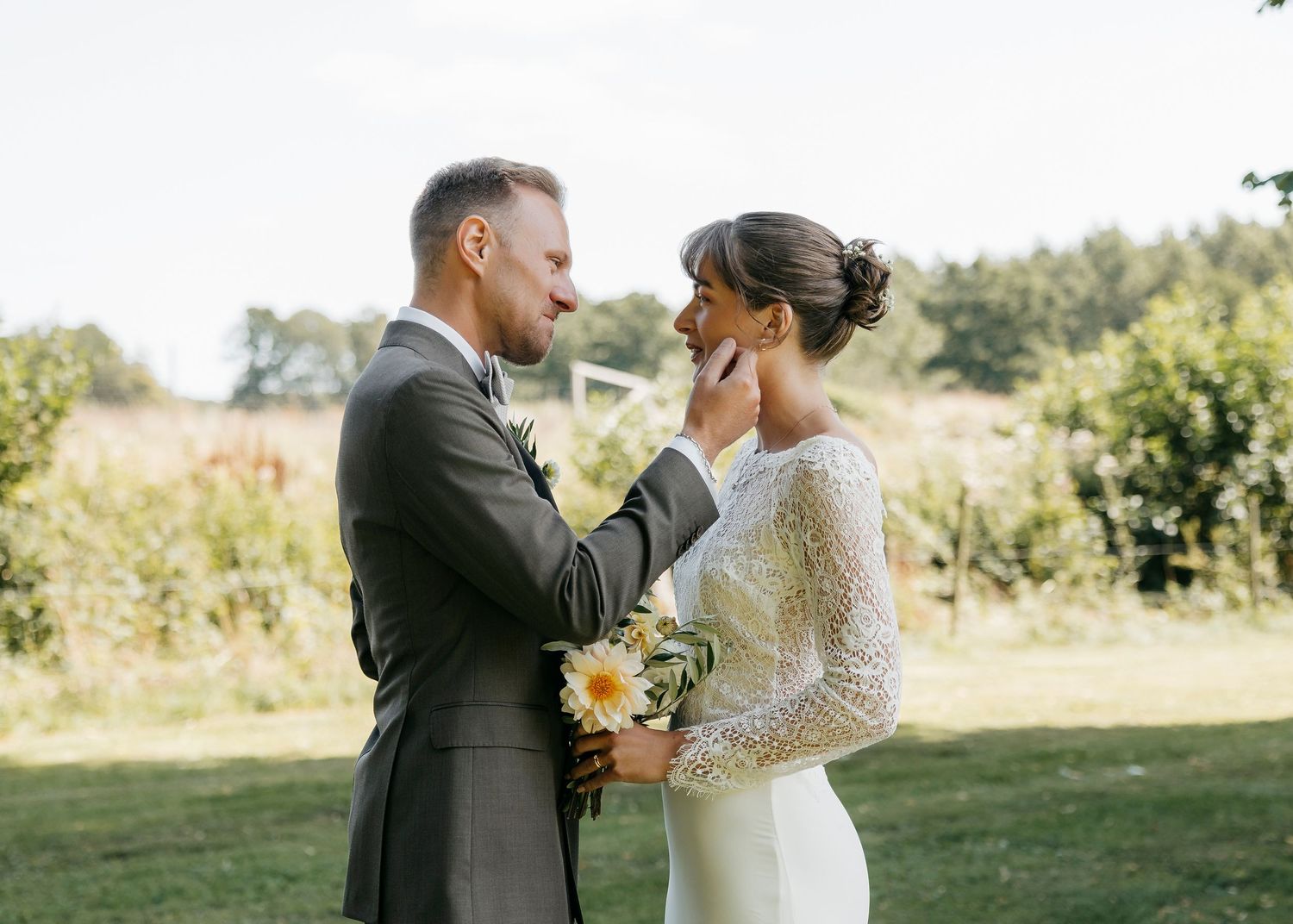 A tender moment between newlyweds holding sunflowers in a rustic outdoor setting.
