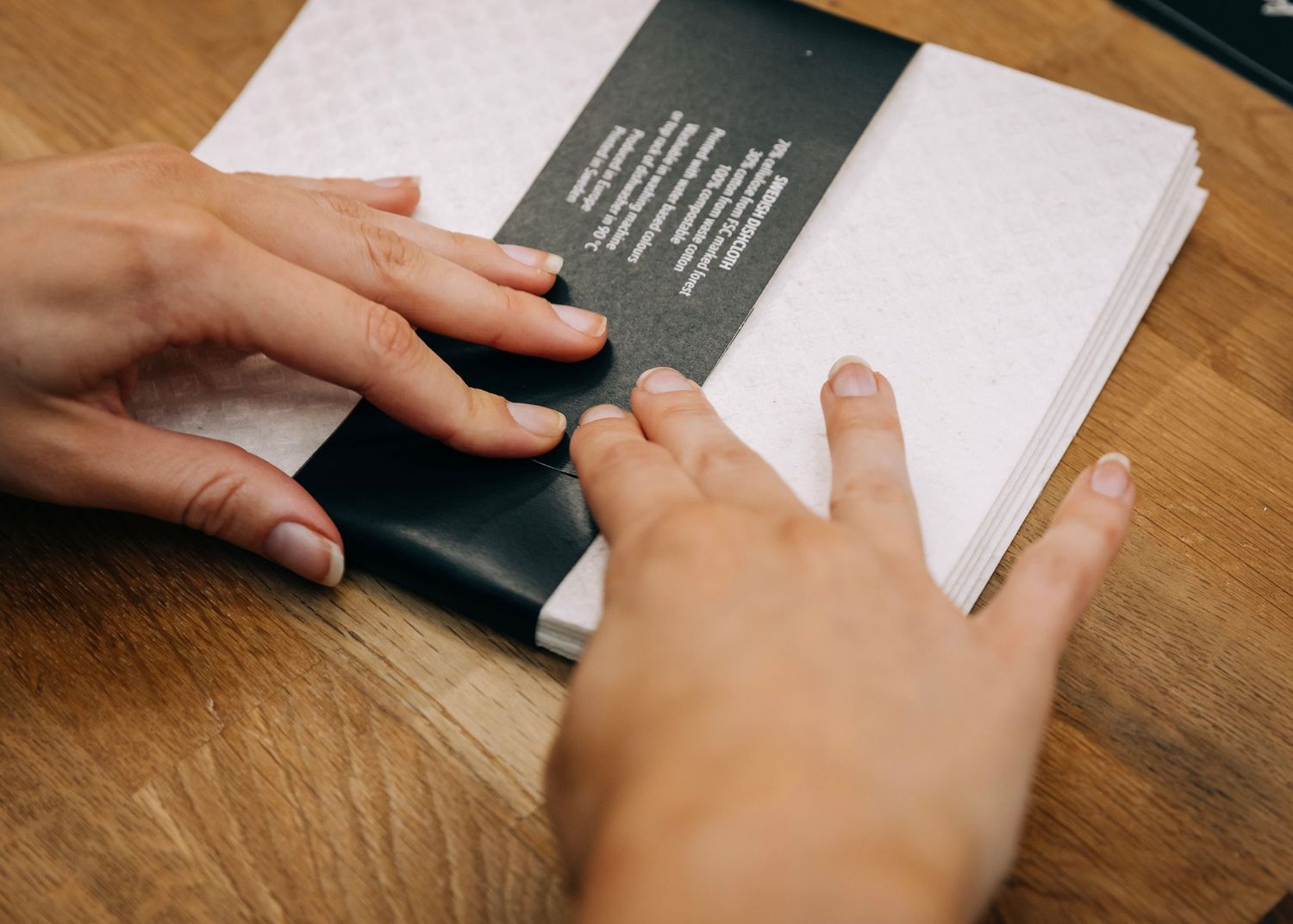 Hands turning pages of a white book or document on wooden surface.