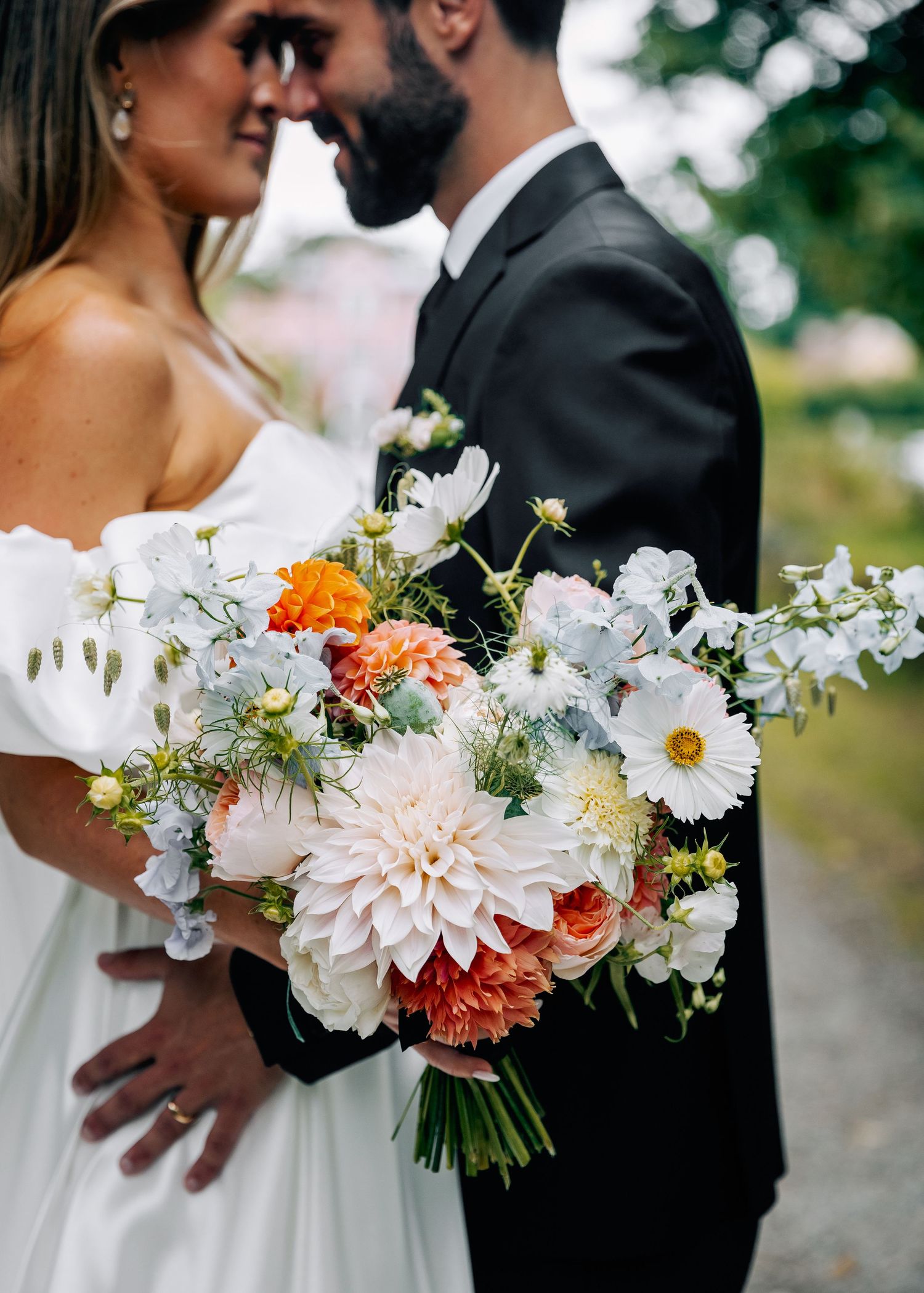 Wedding couple embraces while holding beautiful white and coral floral bouquet.
