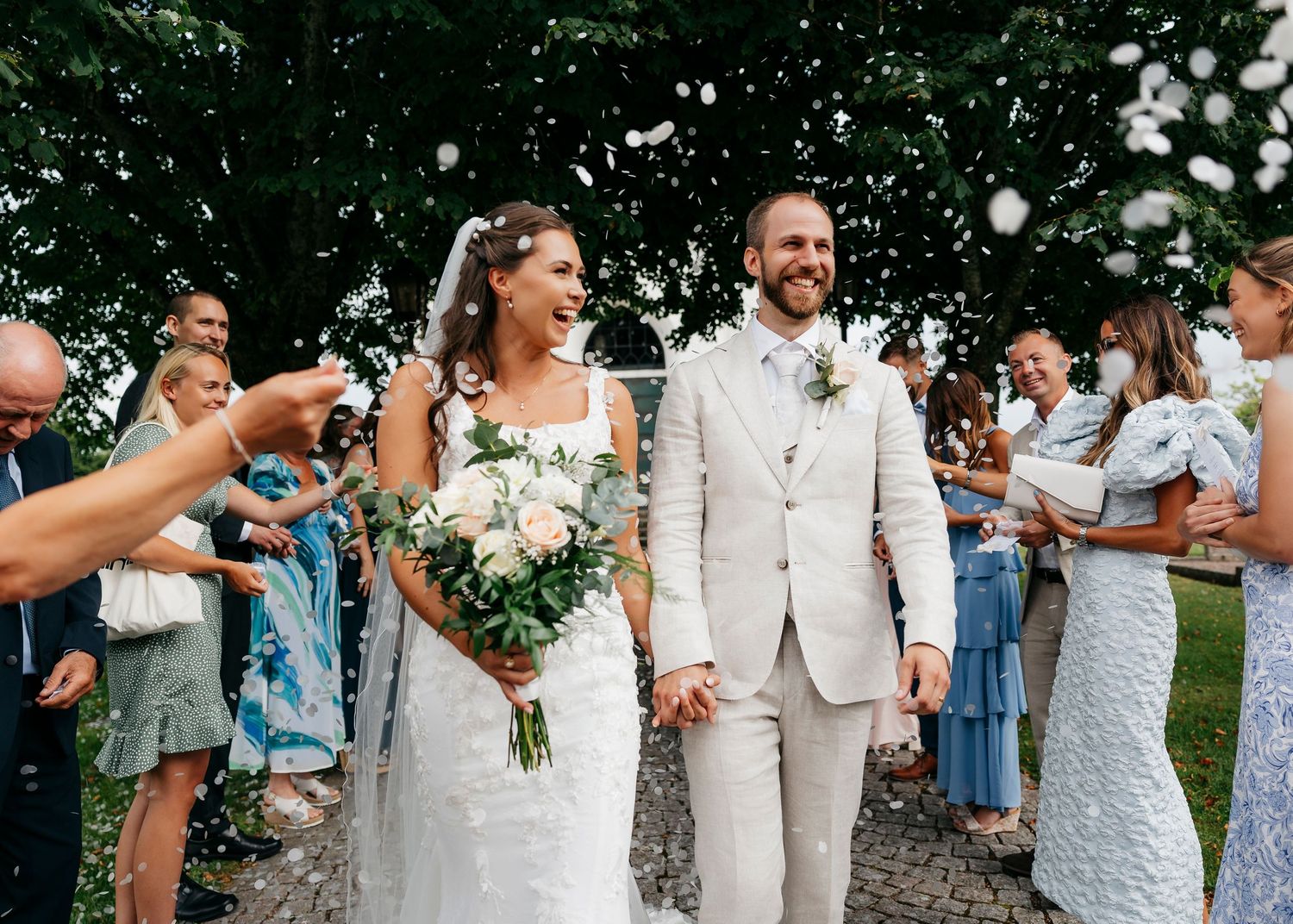 Wedding party celebrating outdoors with confetti and white floral bouquets.