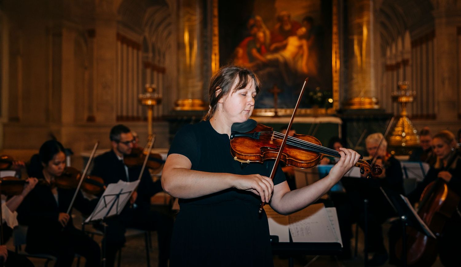 Orchestra performers playing string instruments during a classical concert in an ornate venue.
