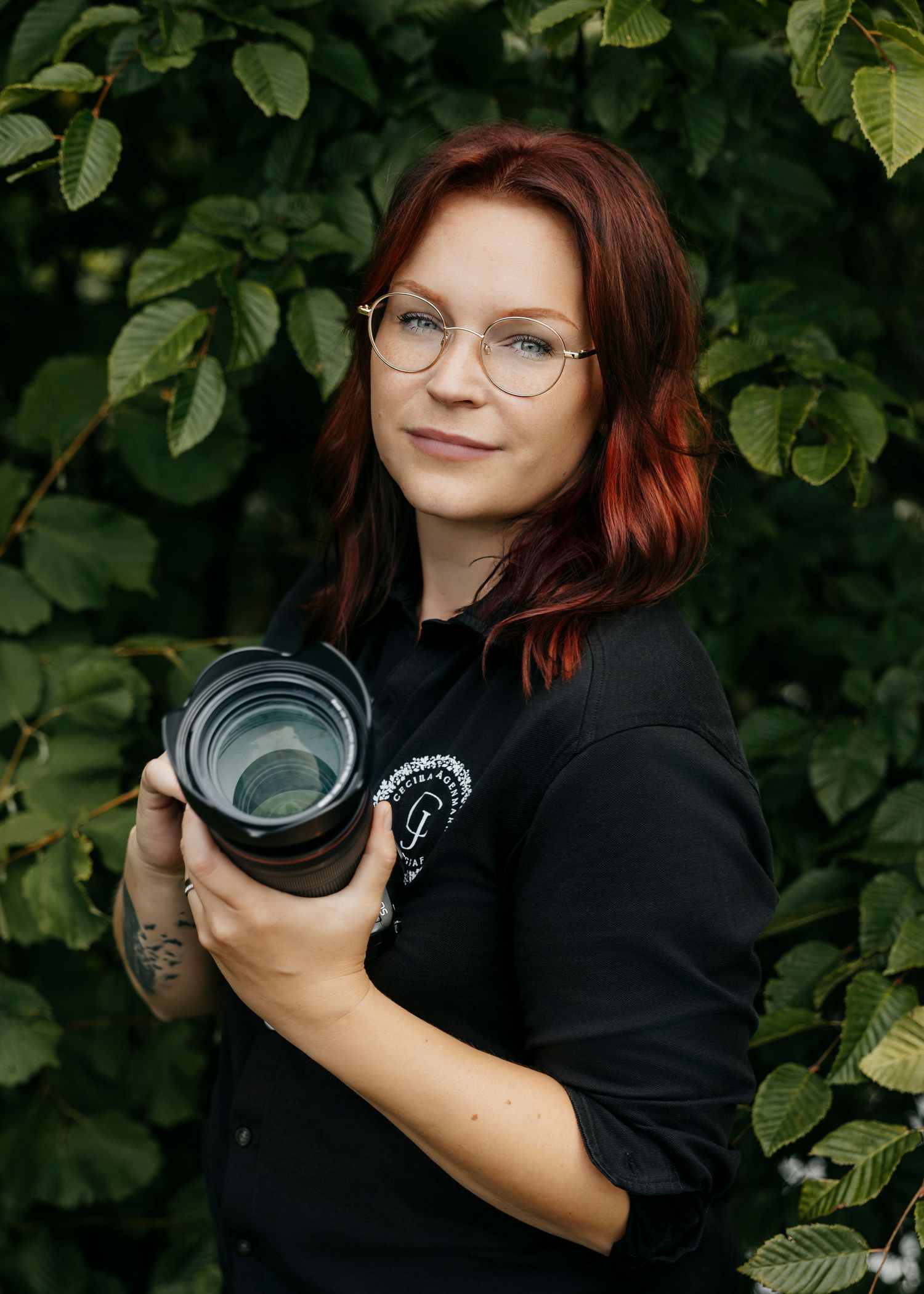 Professional photographer holding camera equipment against green foliage background.