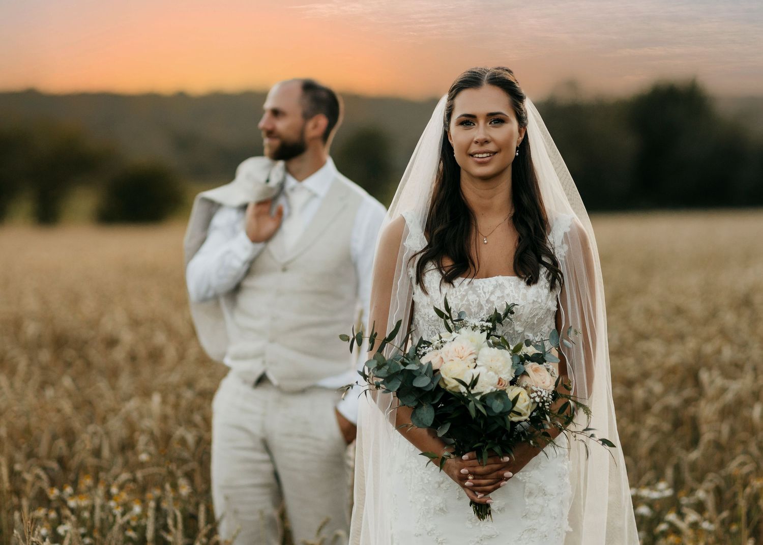 Wedding couple posing in wheat field during sunset with bouquet.