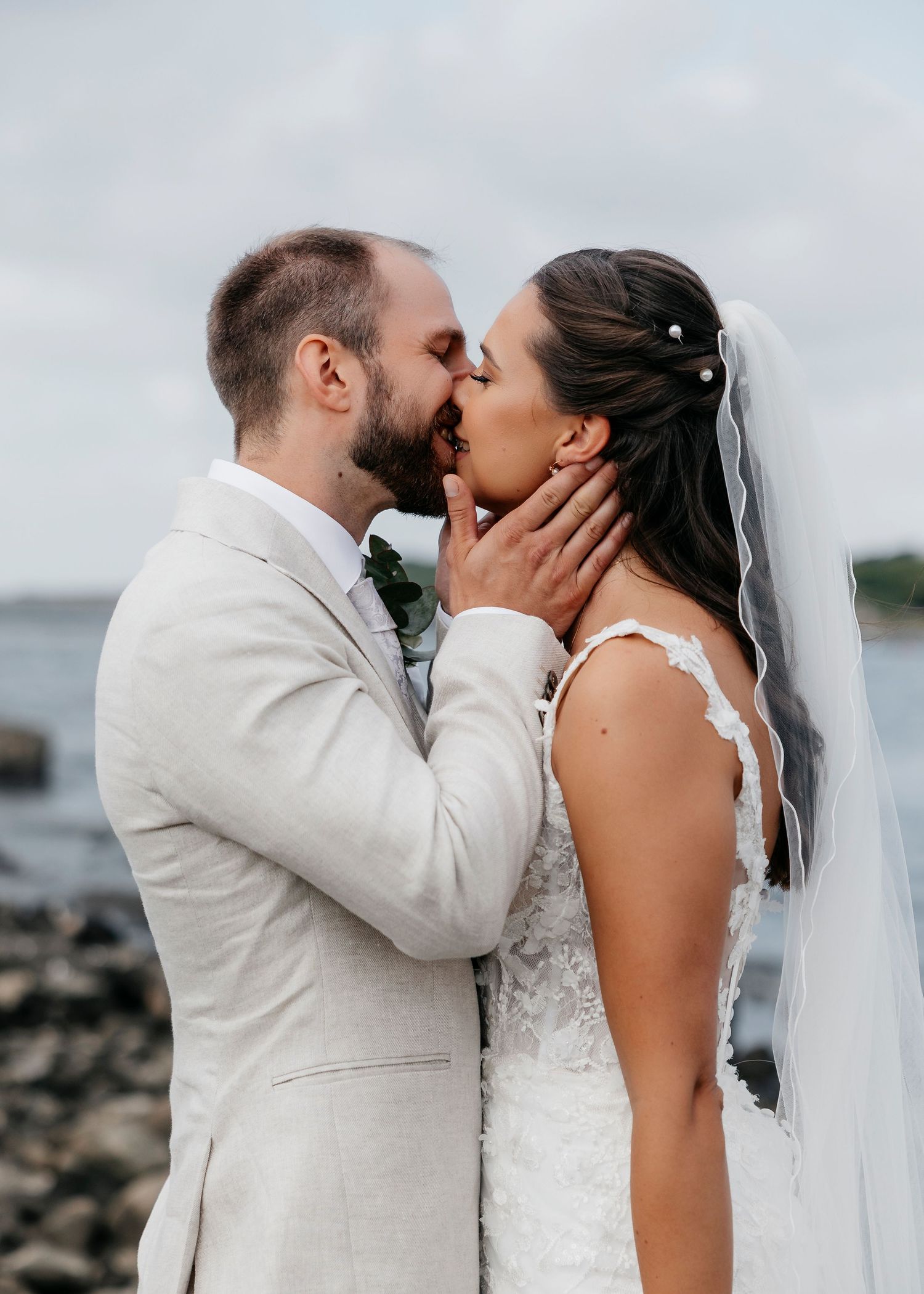Romantic wedding kiss sequence on rocky beach with ocean backdrop.