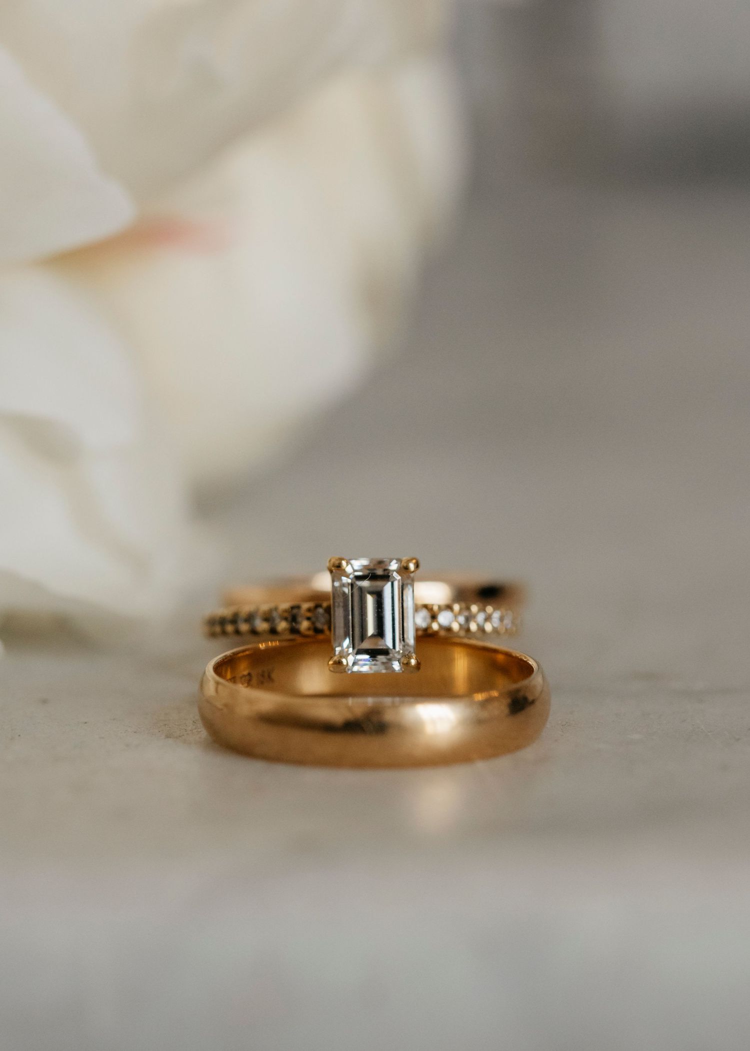 Gold wedding bands and diamond ring arranged with white flowers.
