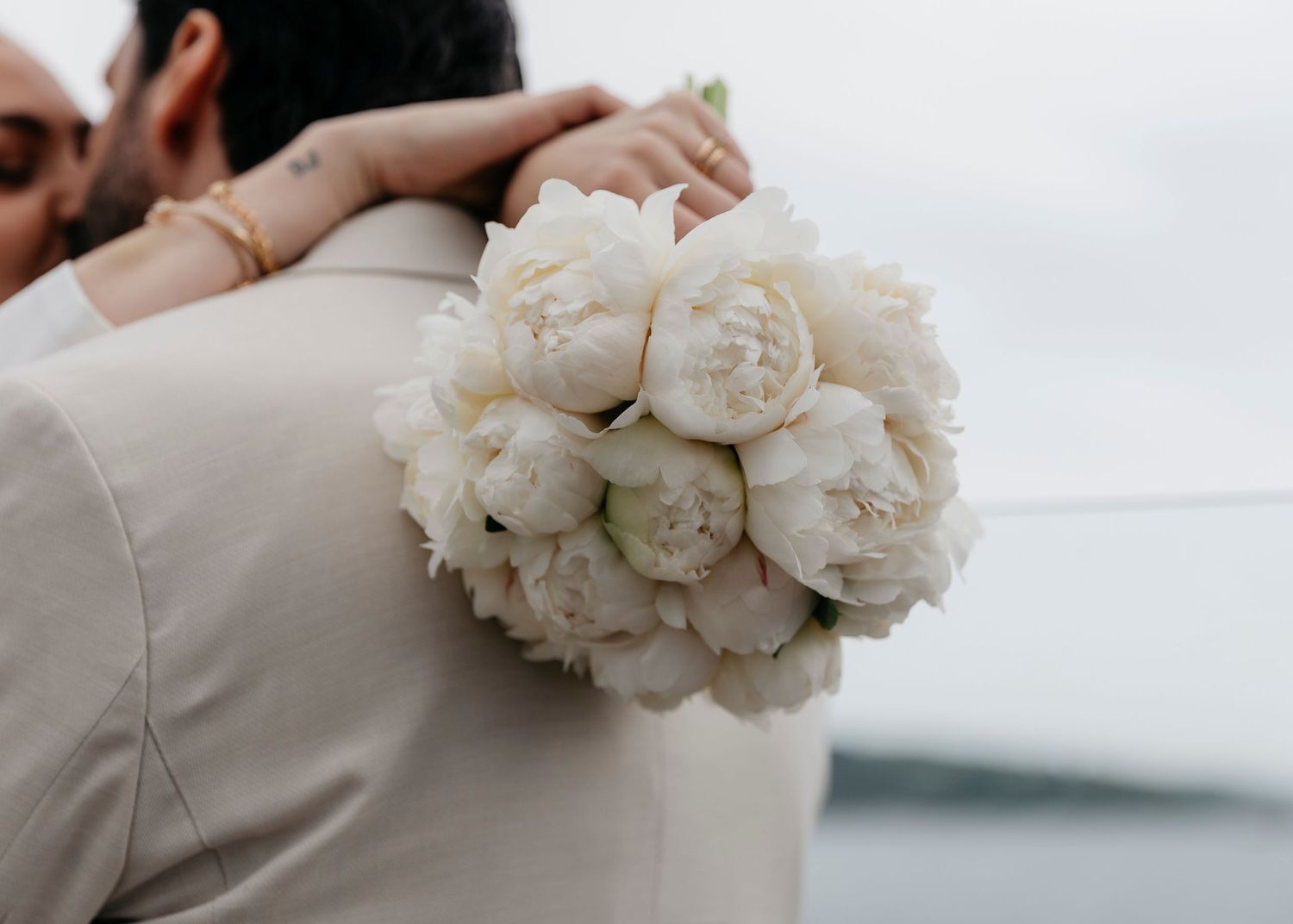 Close-up of white peony bouquet against beige and white wedding attire.