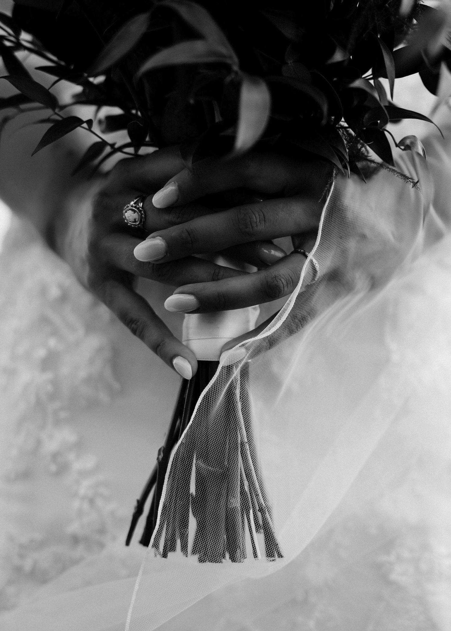Black and white detail shot of hands holding wedding bouquet with flowing veil.