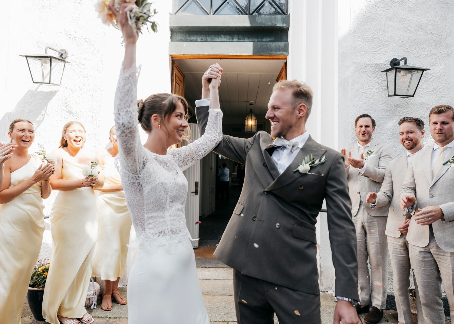 Wedding party celebrates with joyful dancing and laughter in a bright indoor venue.