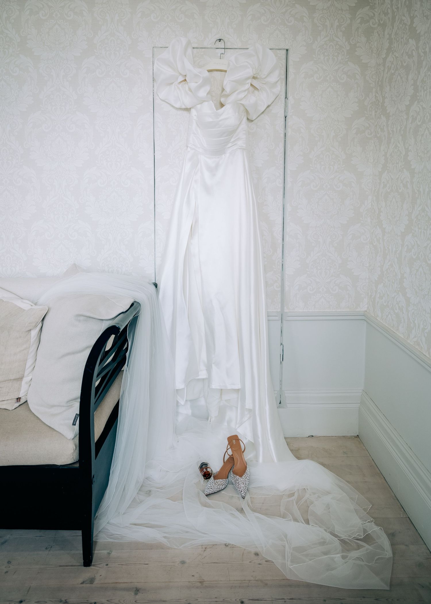 White wedding gown displayed on wall with train flowing onto wooden floor.