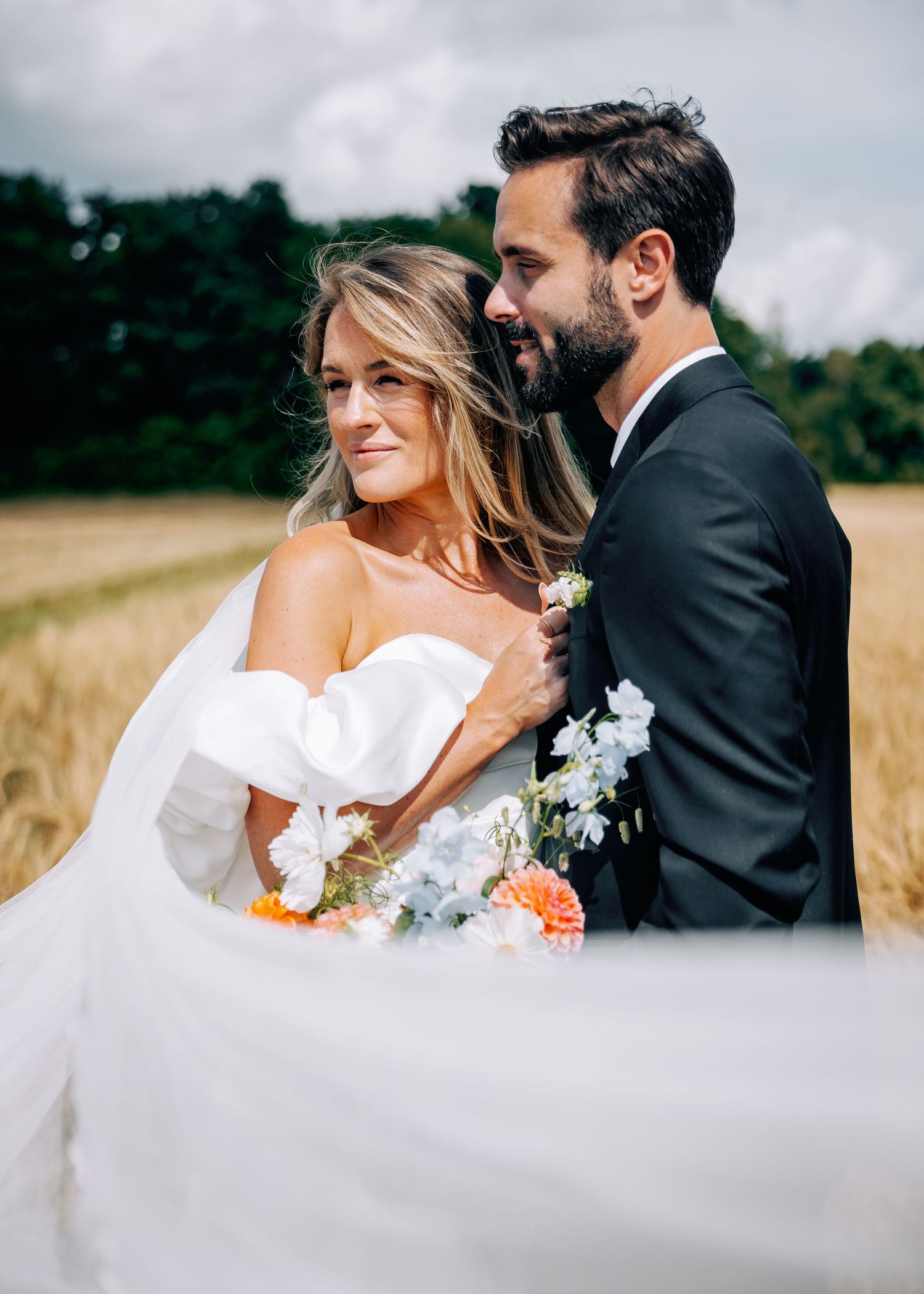 Artistic wedding portraits in wheat field featuring flowing white dress and dramatic sky.