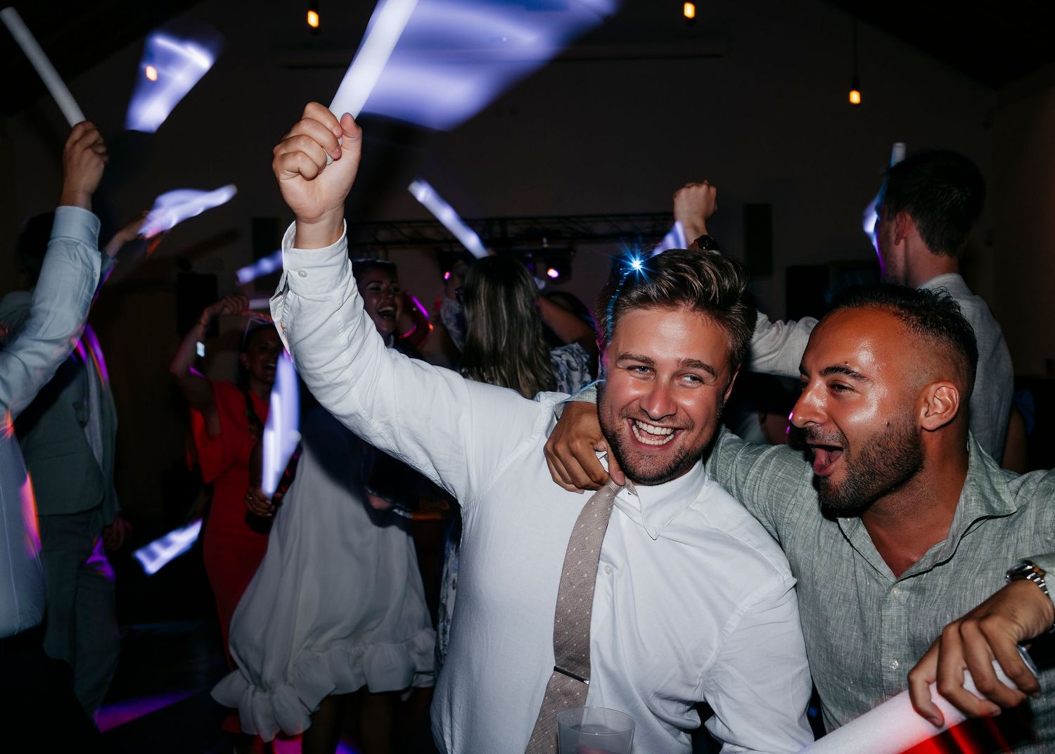 Wedding guests celebrate joyfully with raised arms on a lively dance floor.