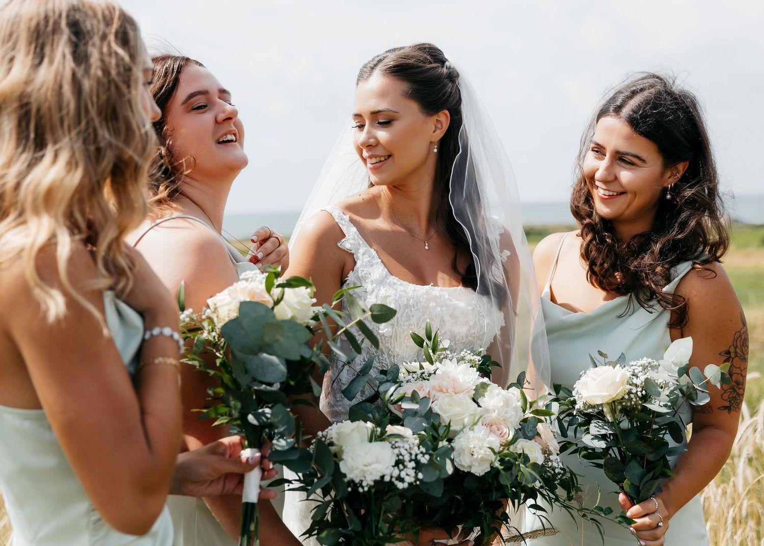 Bridesmaids in light dresses sharing laughs and holding white floral bouquets.