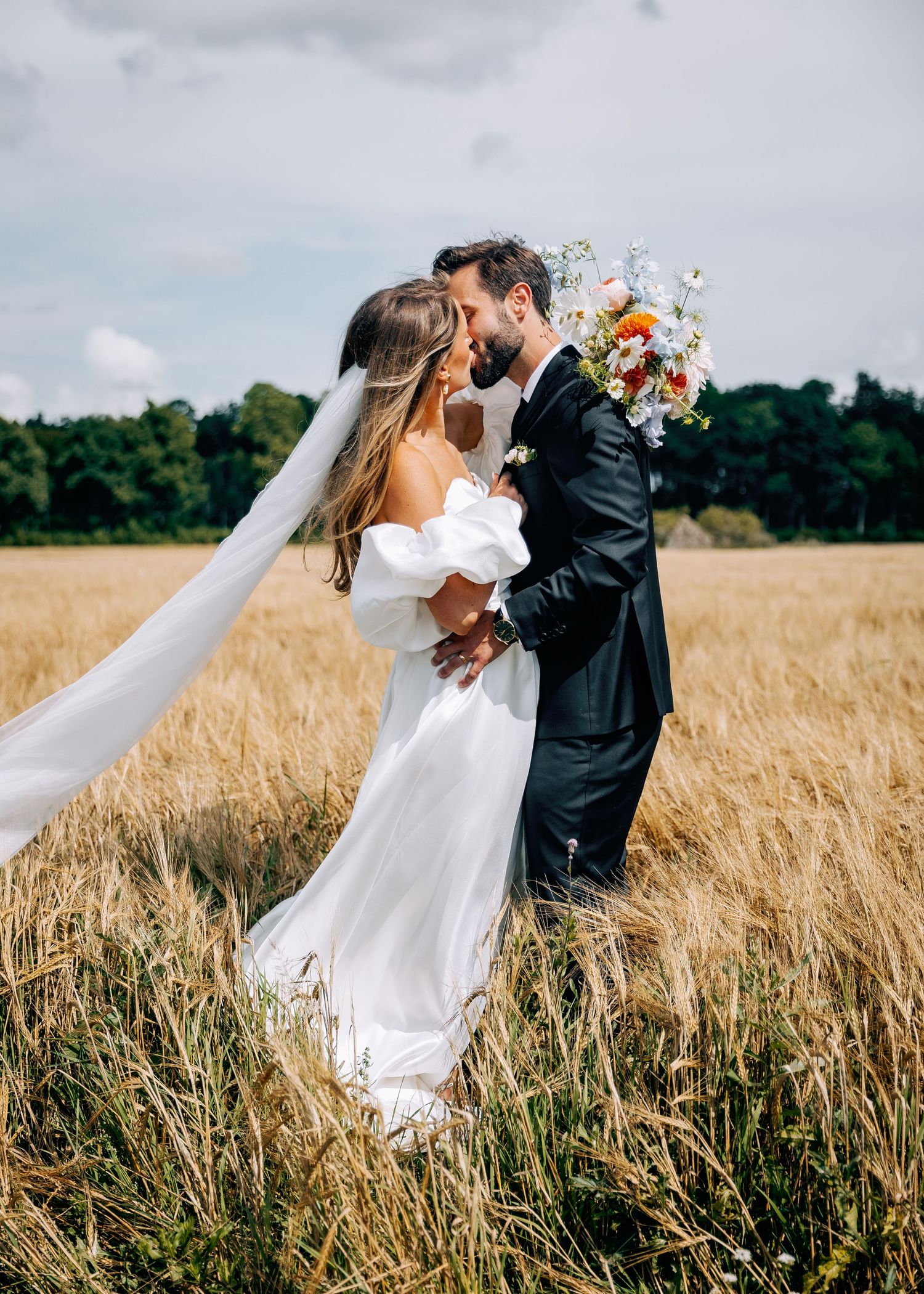 Wedding couple shares romantic moments in a golden wheat field under cloudy skies.