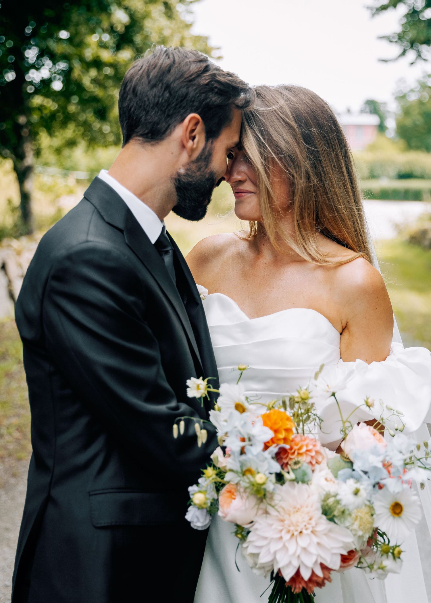 Romantic wedding portraits with white and orange dahlias in the bouquet against natural outdoor setting.